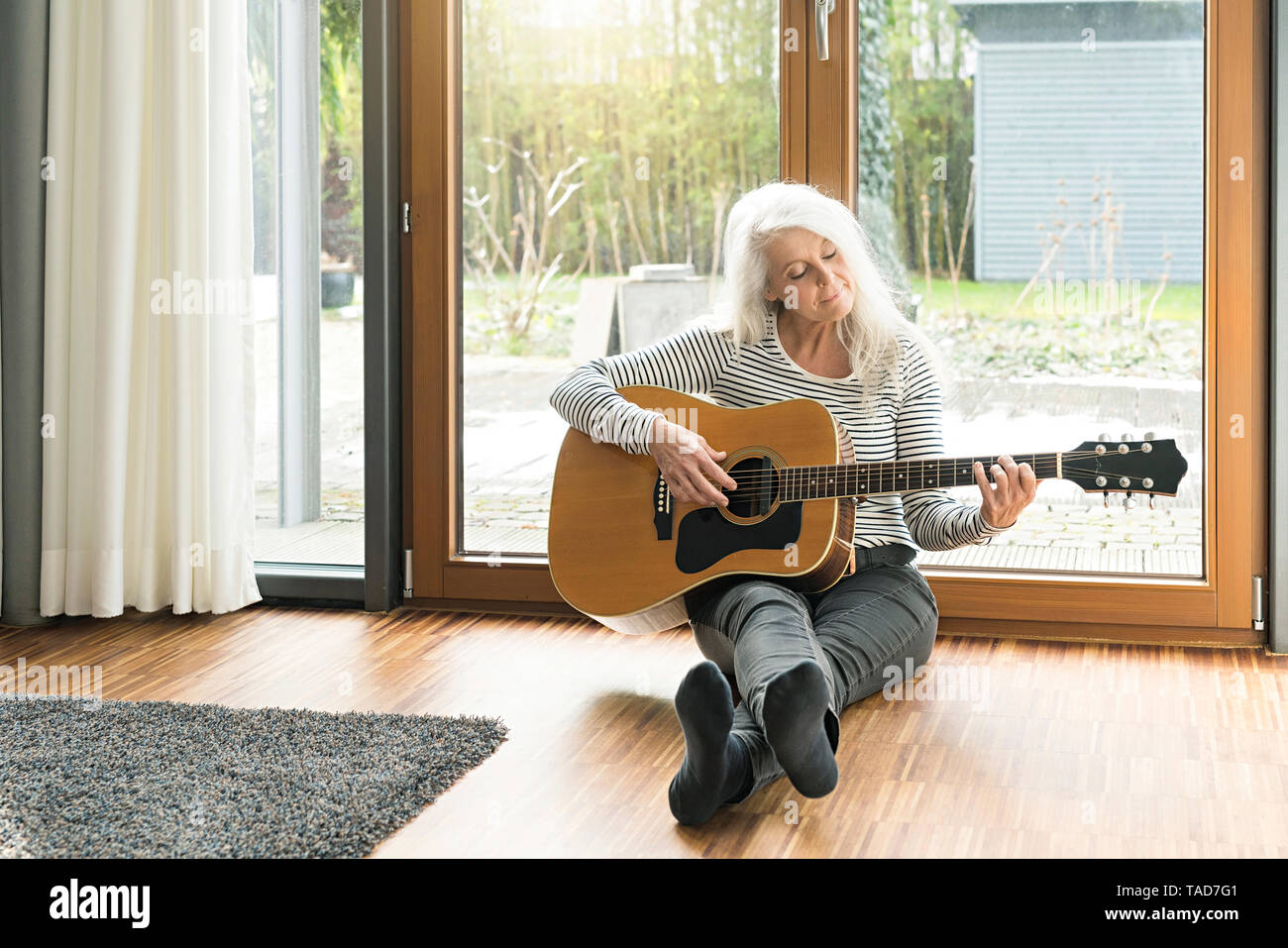 Couple assis sur le plancher de salle de séjour qui joue de la guitare Banque D'Images
