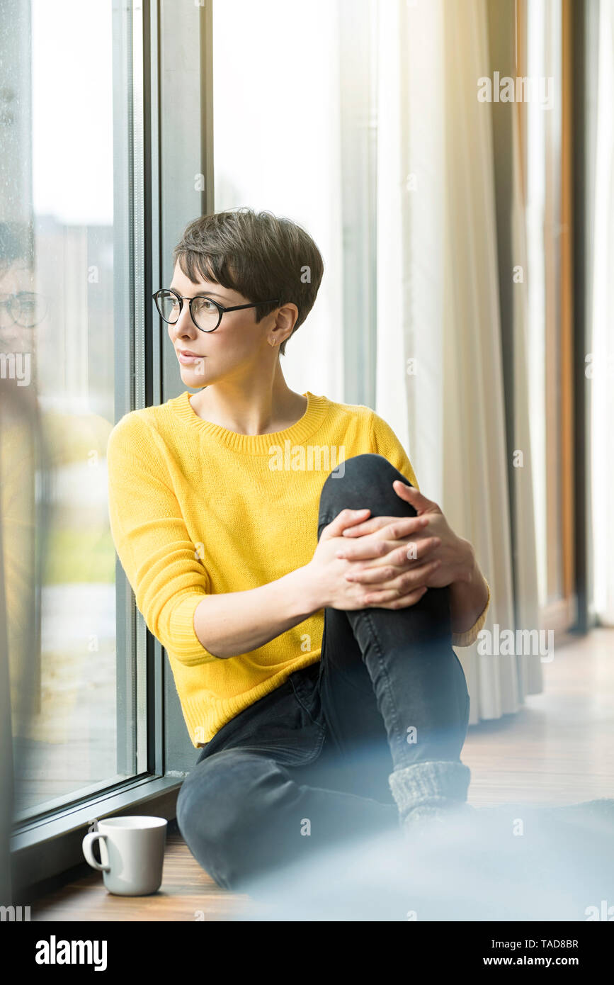 Portrait de femme avec tasse de café assis sur le plancher à la maison à la fenêtre de Banque D'Images