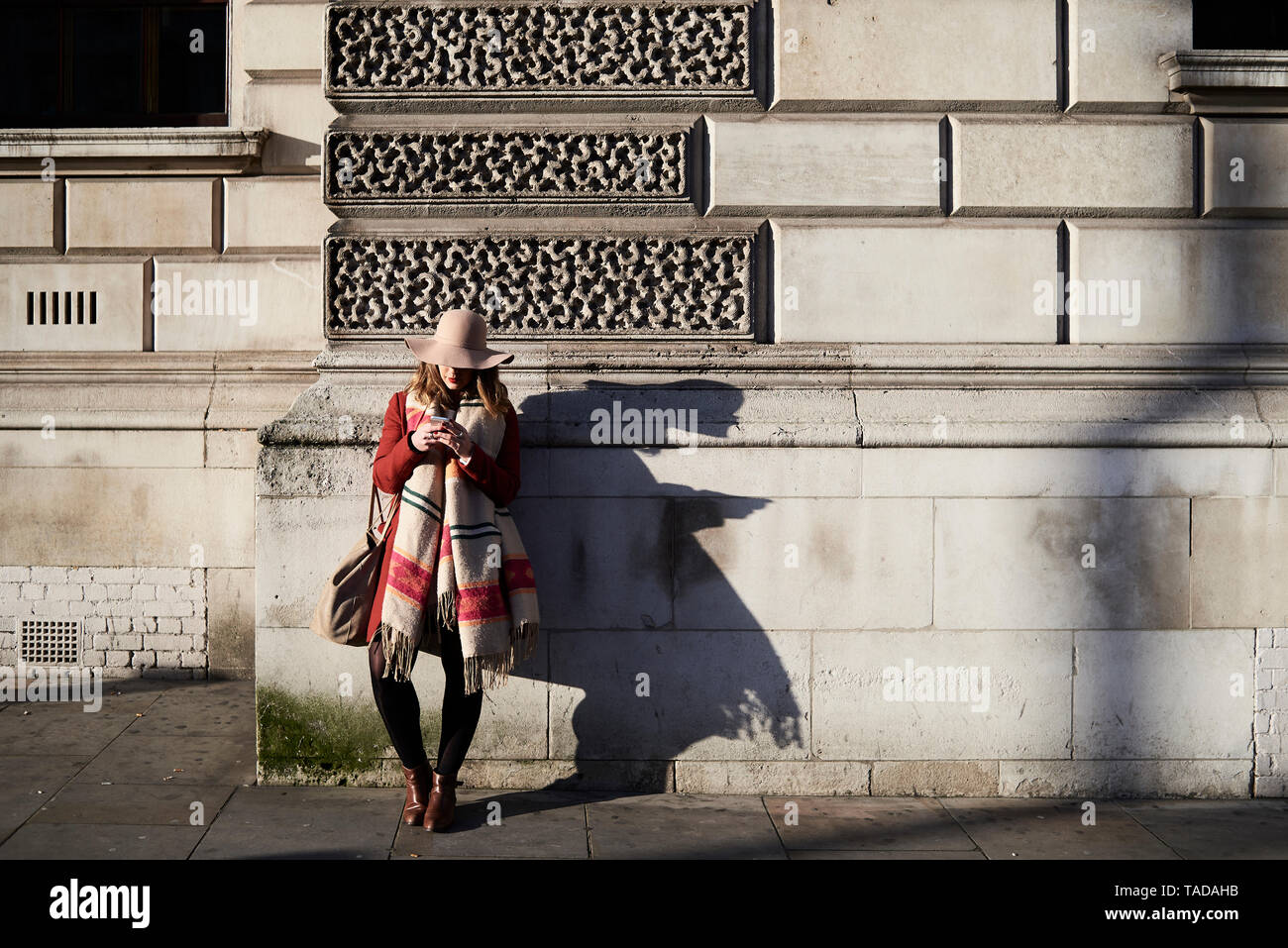 Femme élégante debout à un bâtiment using cell phone Banque D'Images