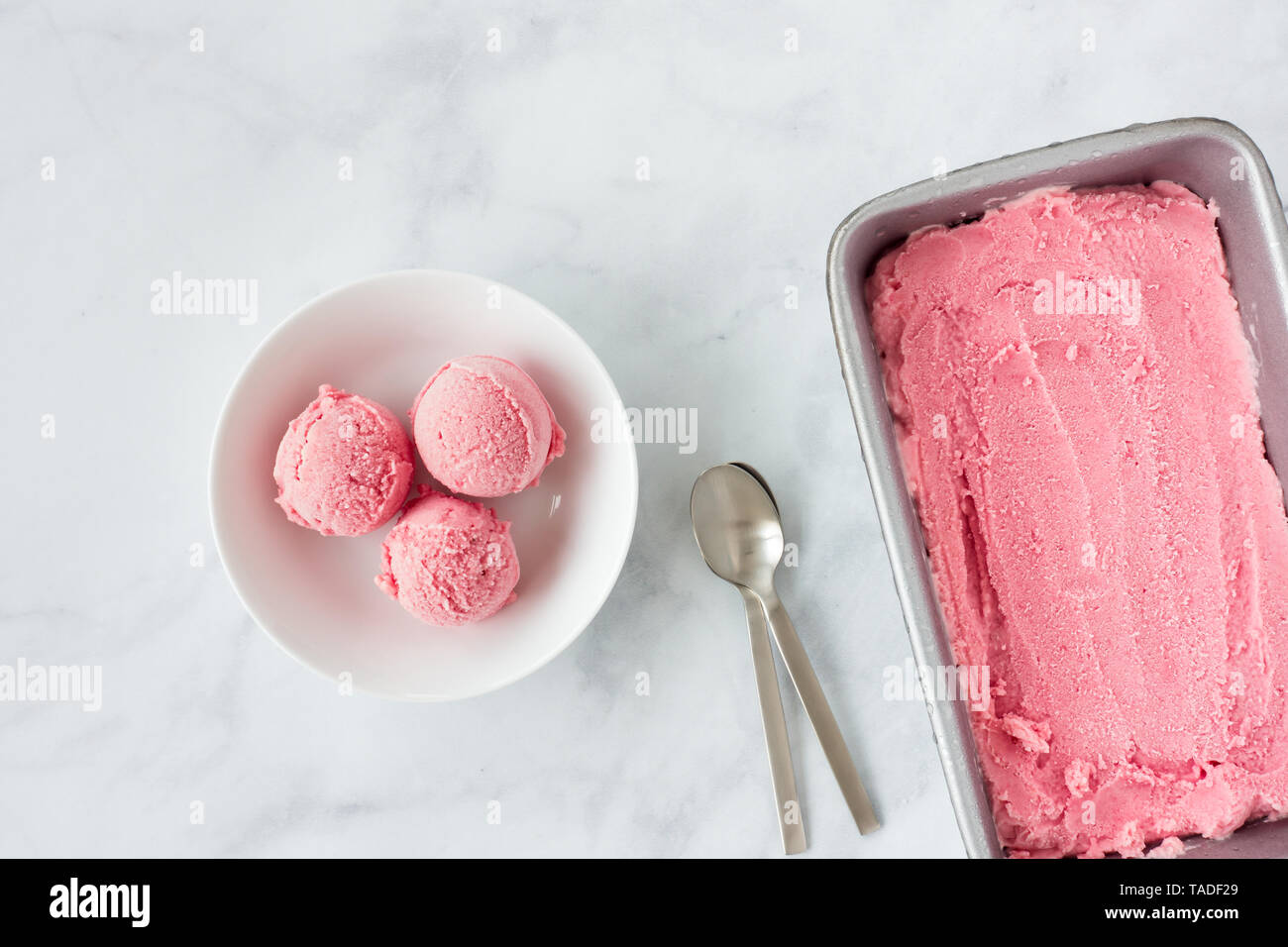 La rhubarbe forcée rose crème de glace dans le récipient et bol avec des cuillères sur fond de marbre blanc avec l'exemplaire de l'espace. Vue d'en haut. Banque D'Images