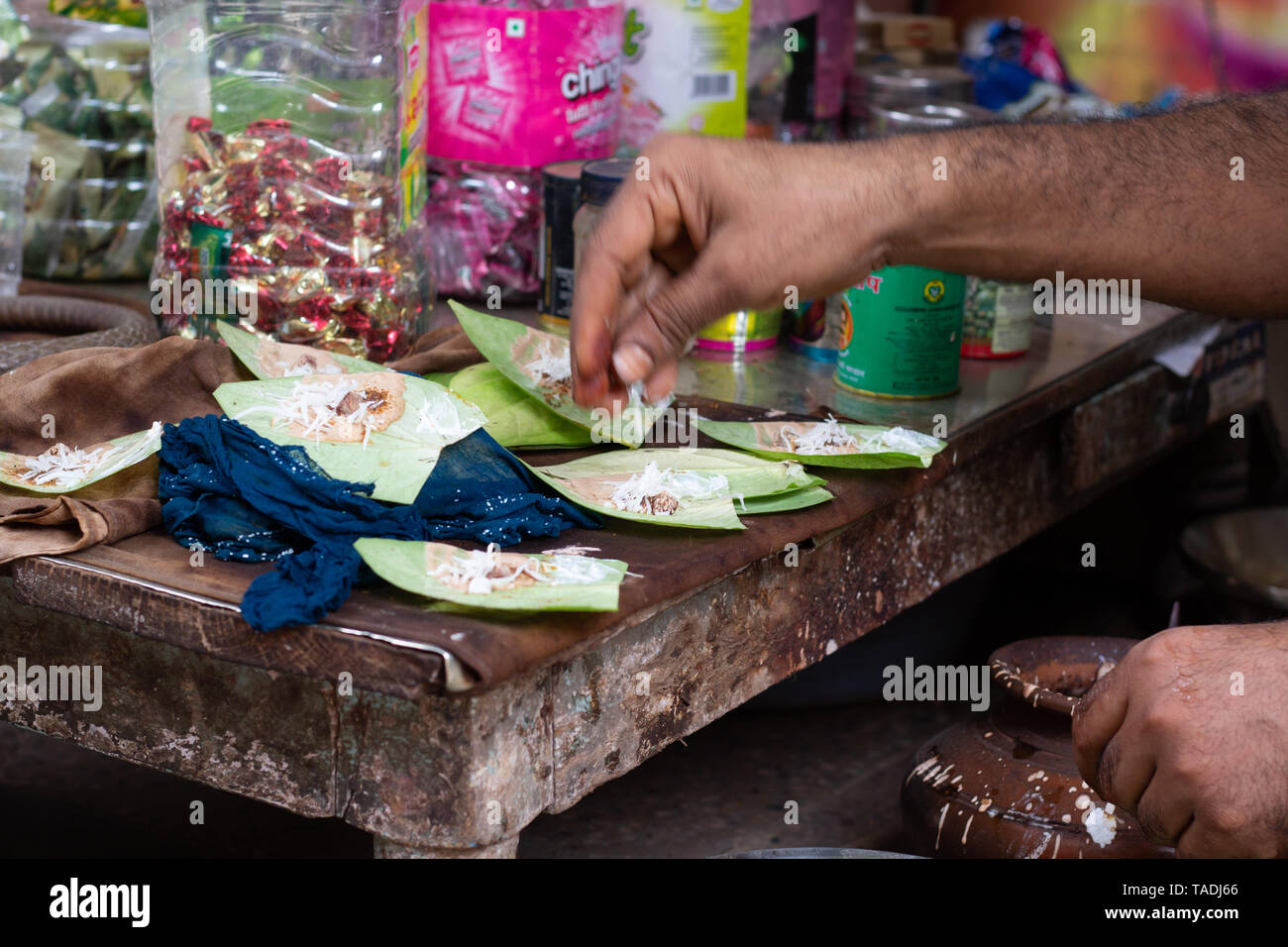 Préparation de paan doux au stand de la rue dans les rues de Varanasi, en Inde. Un homme se mélange de noix de coco râpée, pâte de menthe et d'autres ingrédients sur la feuille de bétel. Banque D'Images