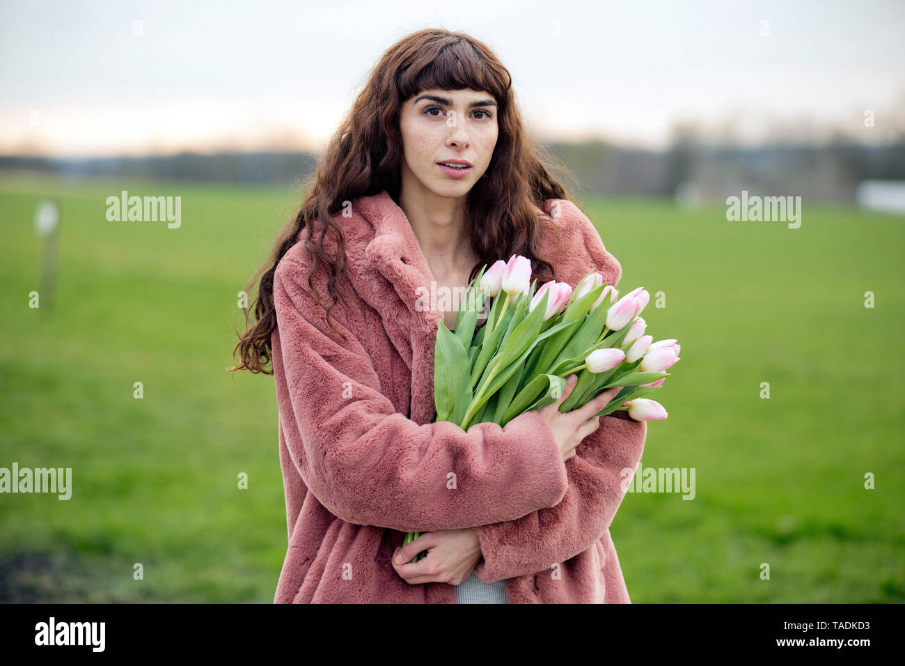 Jeune femme avec bouquet de tulipes et manteau rose Banque D'Images