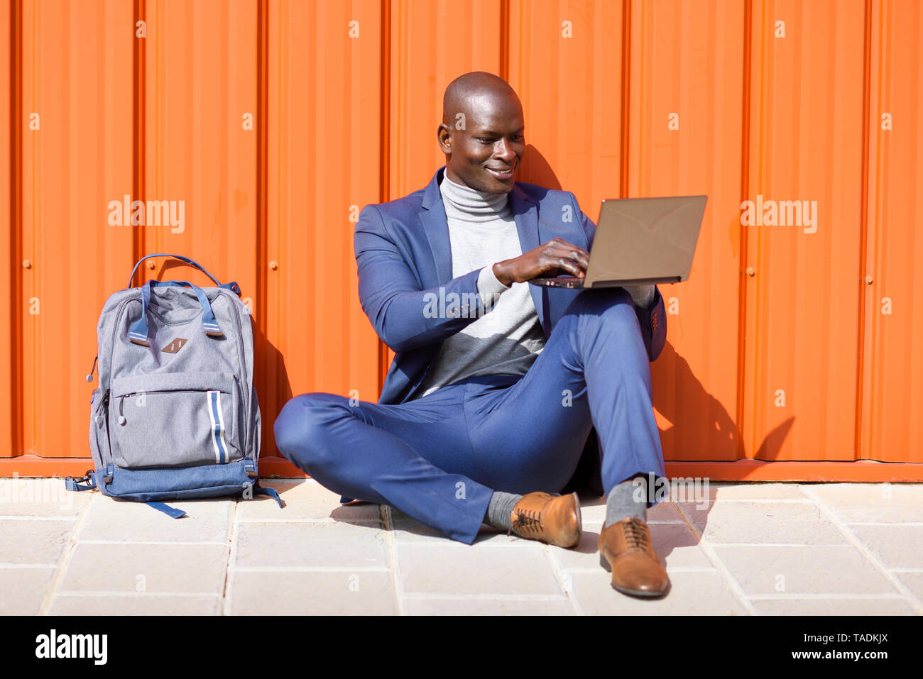 Mode portrait orange wall using laptop Banque D'Images