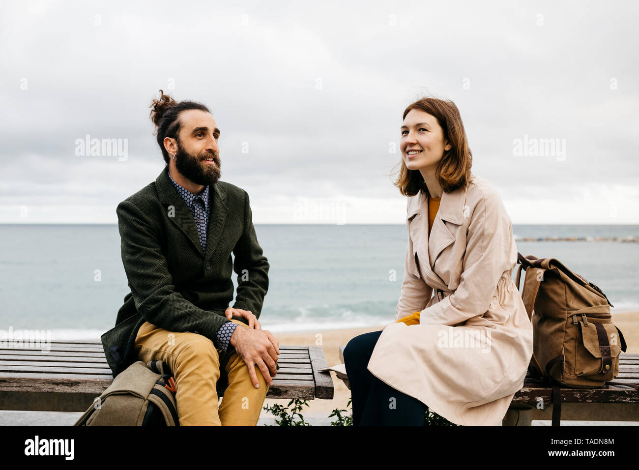 Smiling couple assis sur un banc de la promenade de la plage à parler Banque D'Images