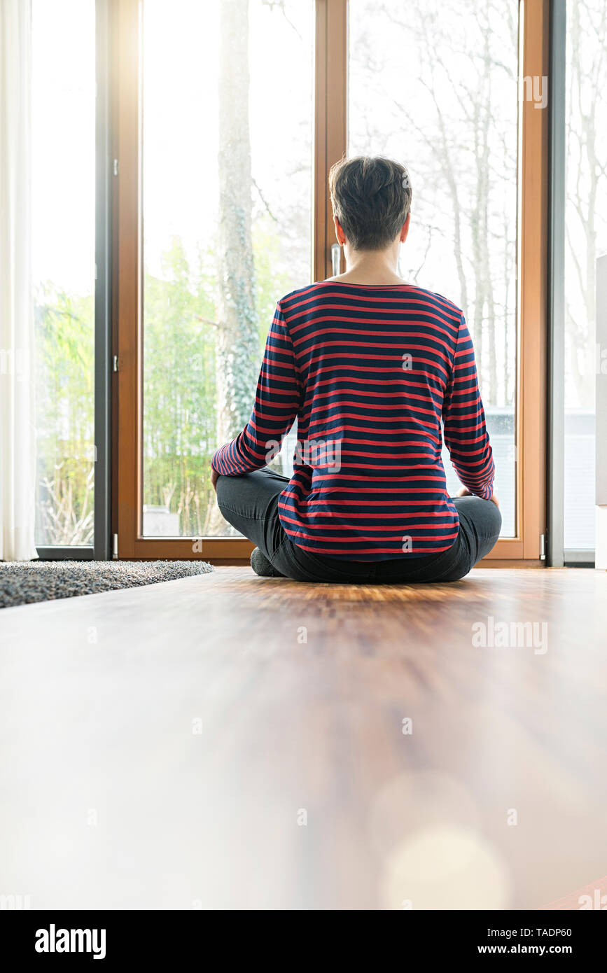 Vue arrière de femme assise sur le plancher de salle de séjour méditer Banque D'Images