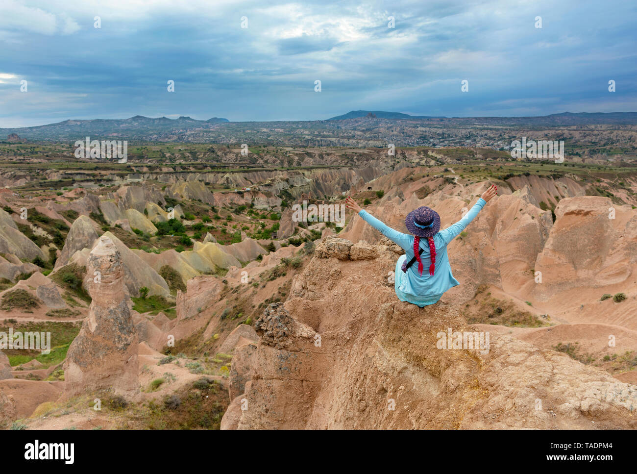 Une jeune fille en vêtements turquoise se trouve au sommet d'un rocher en Cappadoce et se répandre ses bras sur montagnes, ravins et un ciel bleu. Banque D'Images