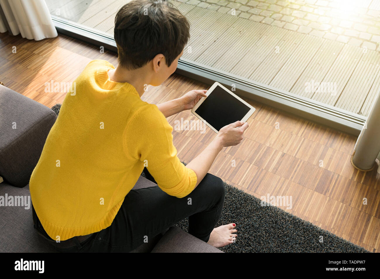 Femme assise sur le canapé dans le salon looking at digital tablet Banque D'Images