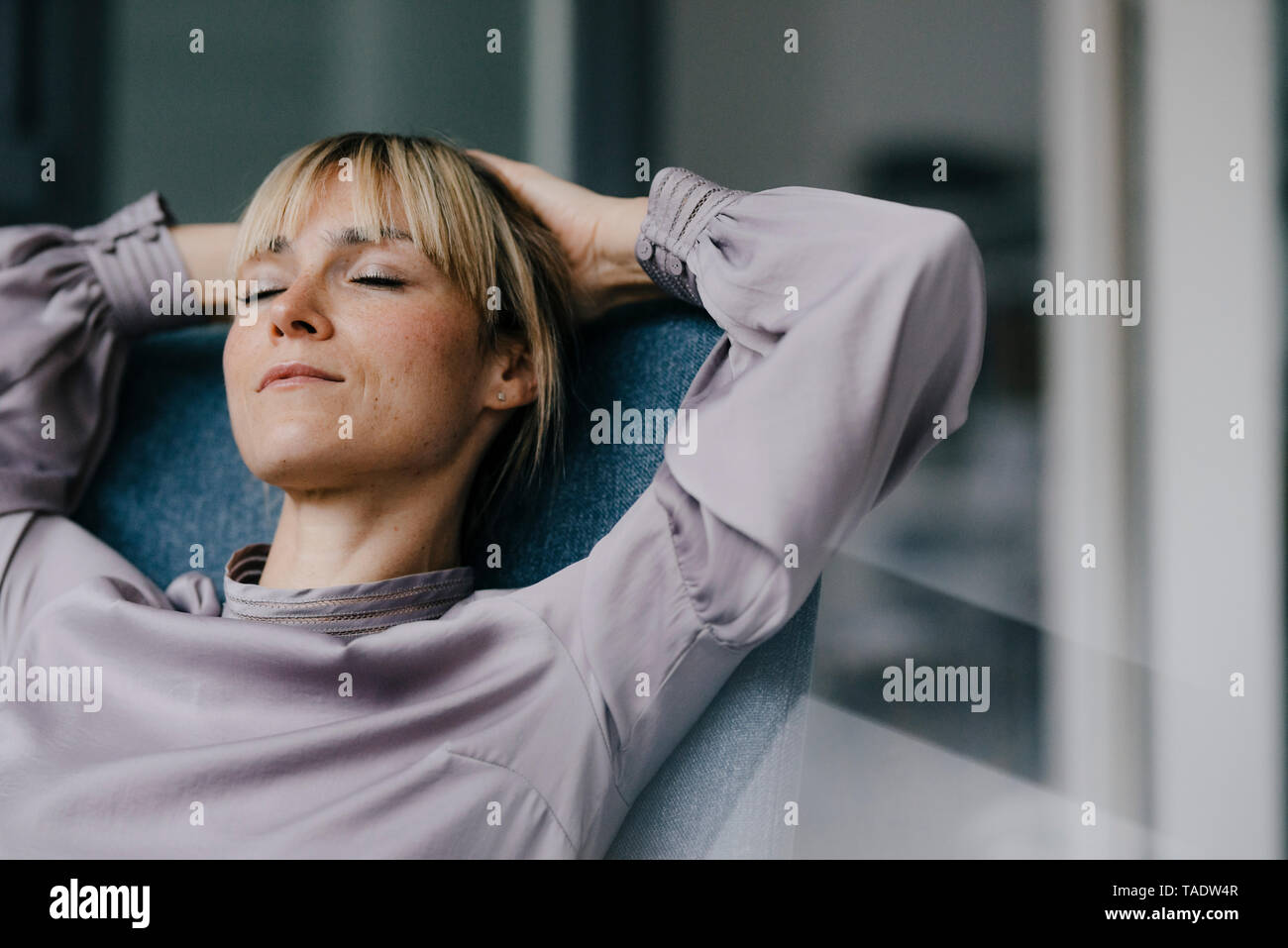 Blonde woman relaxing in armchair, avec les mains derrière la tête Banque D'Images