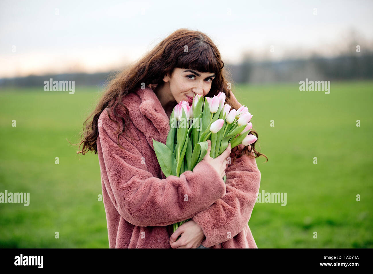 Jeune femme avec bouquet de tulipes et manteau rose Banque D'Images