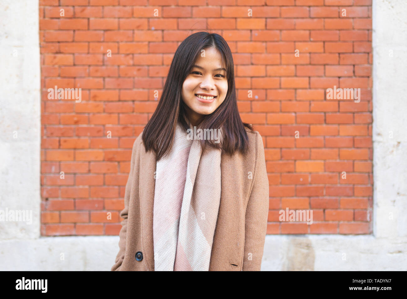 Portrait of smiling young woman at brick wall Banque D'Images