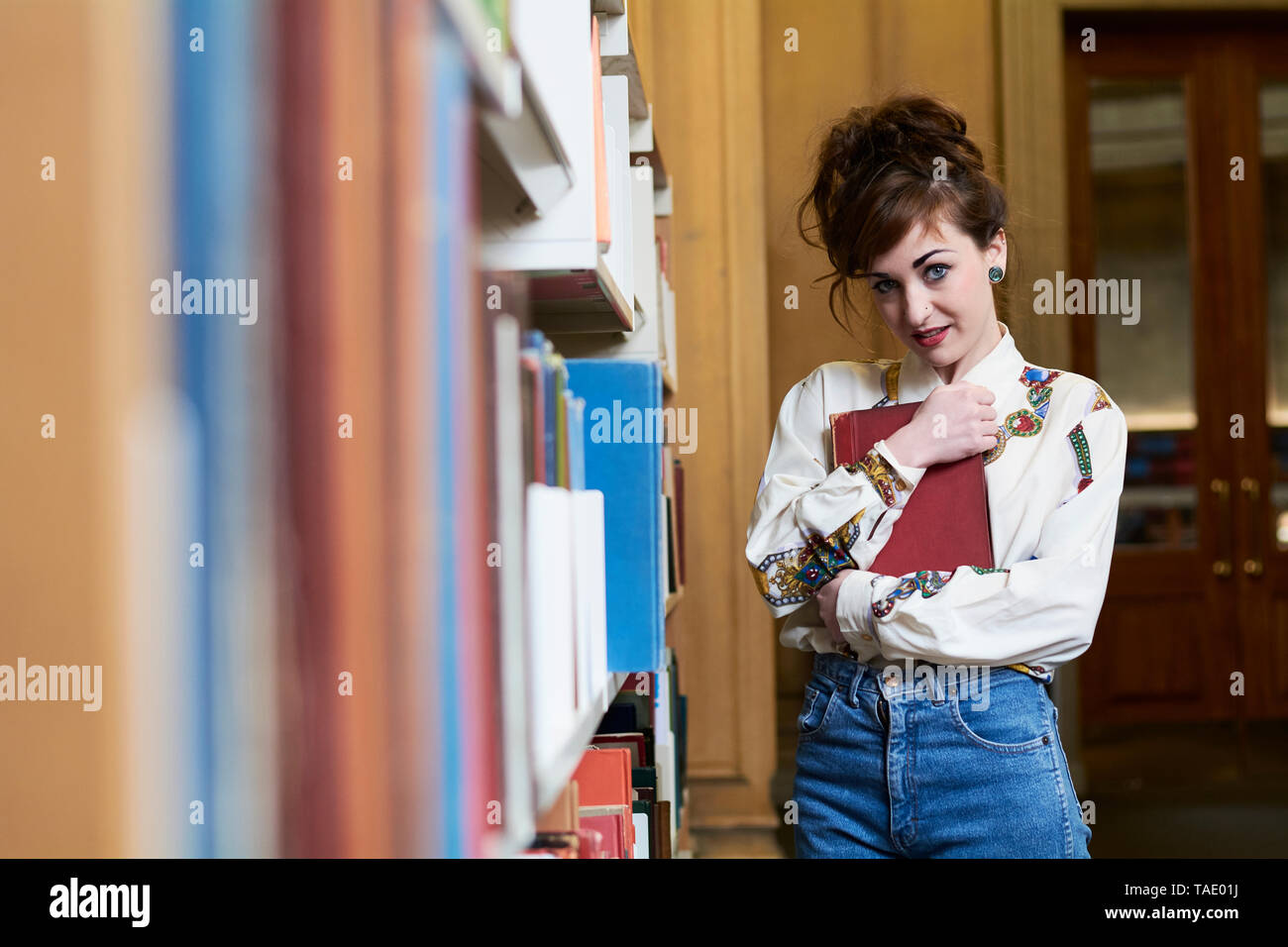 Female student holding un livre dans une bibliothèque publique Banque D'Images