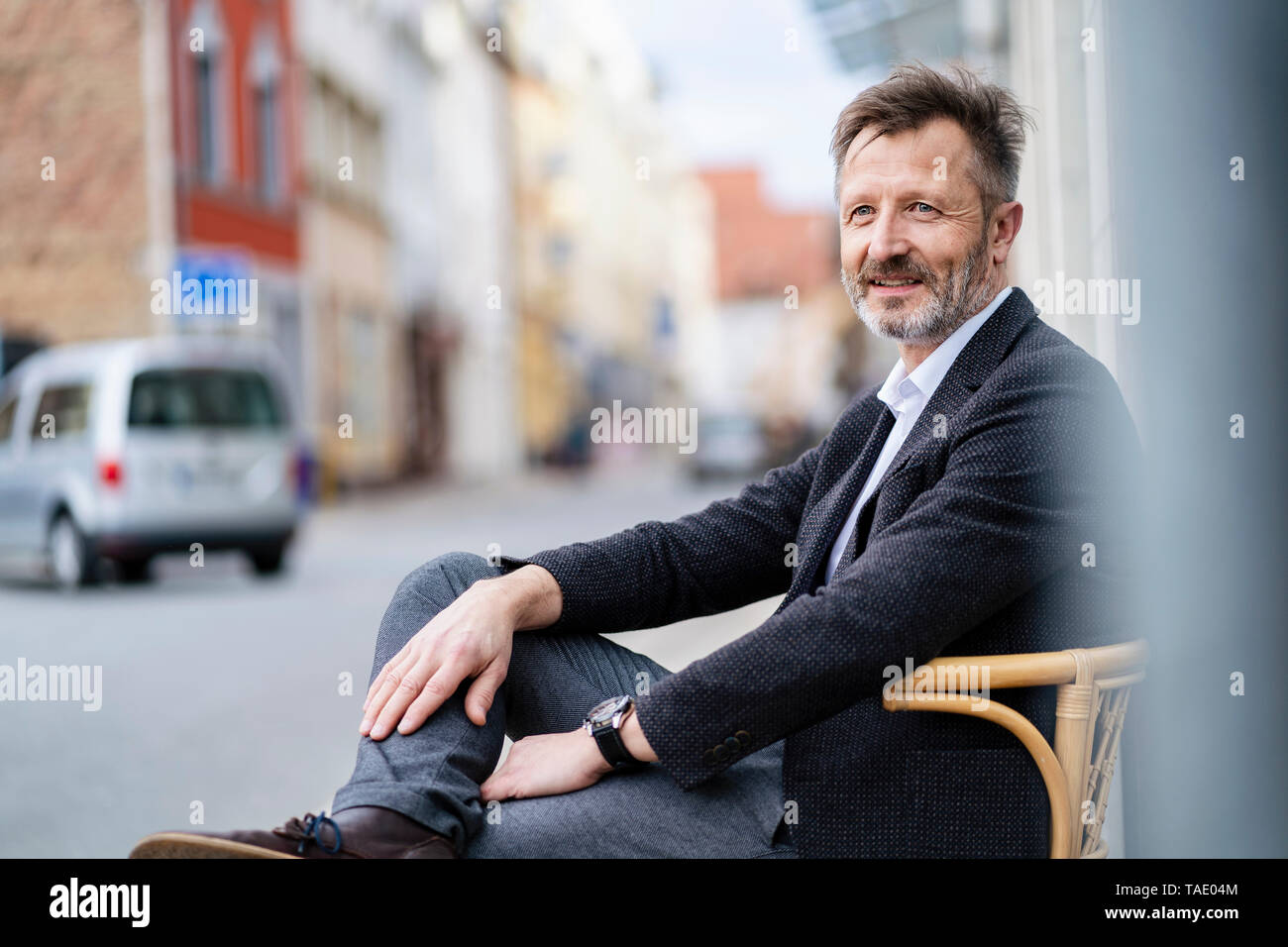 Portrait de contenu mature businessman avec barbe grisonnants assis sur une chaise dans la ville Banque D'Images