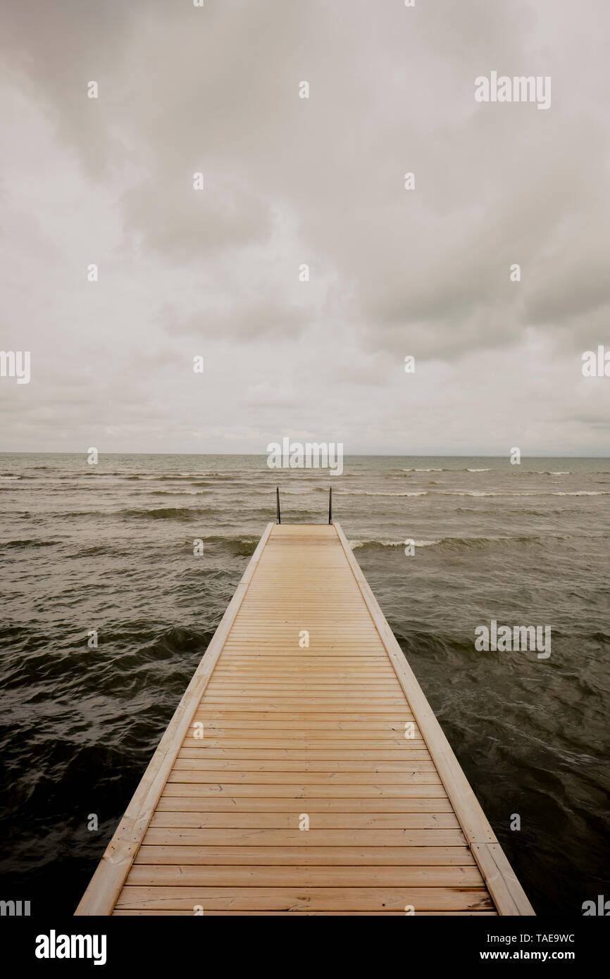 Un caillebotis vide pier menant à la mer dans un ciel nuageux gris Banque D'Images