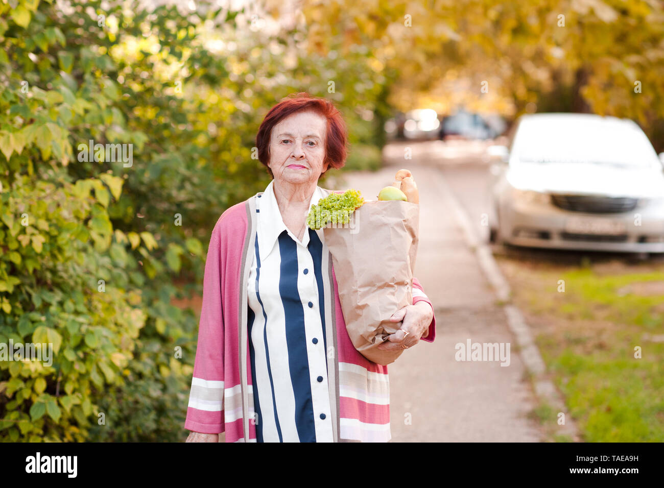 Fatigué senior woman 70-80 ans holding sac avec de la nourriture à la maison à l'extérieur. En regardant la caméra. Banque D'Images
