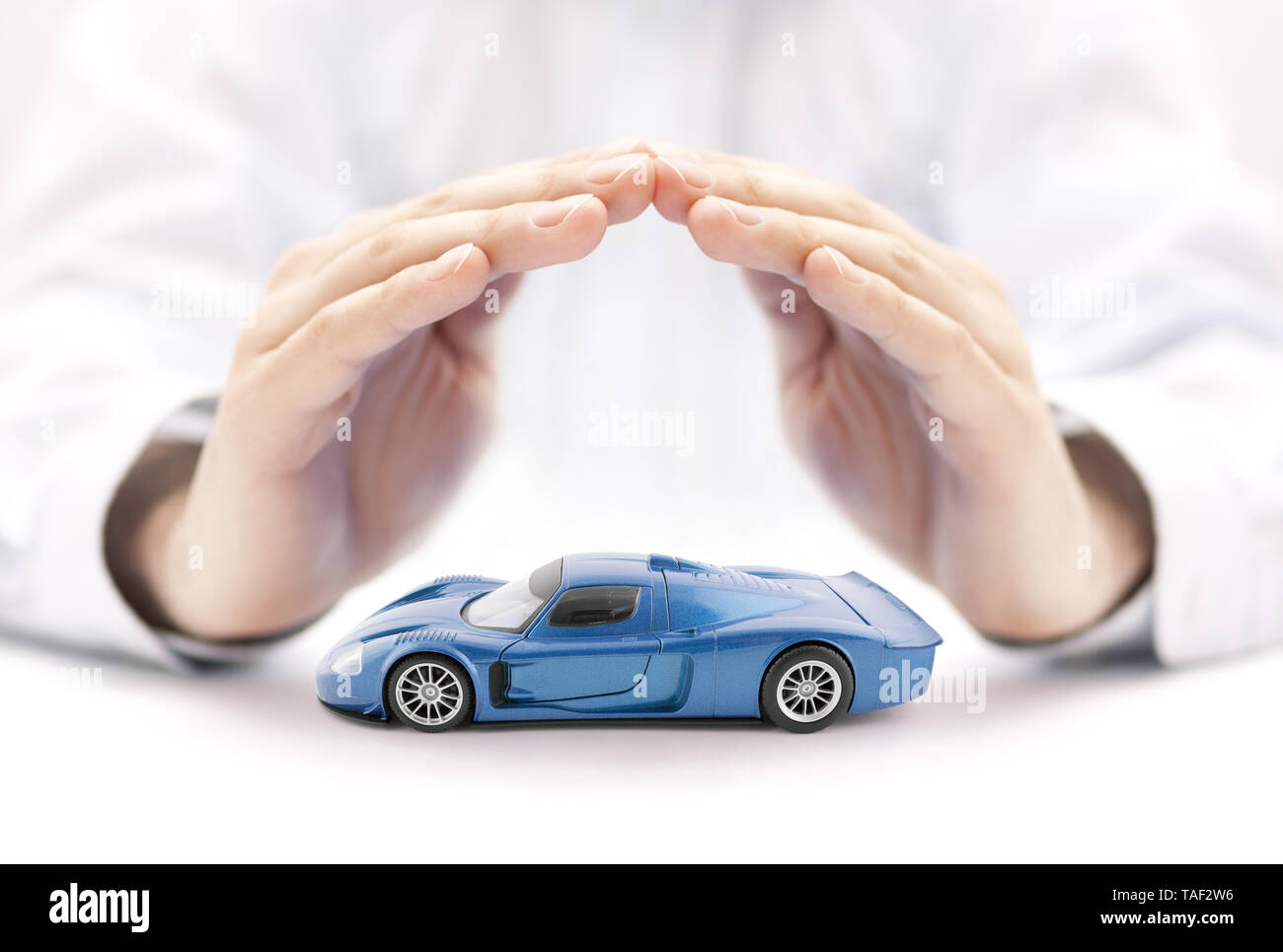 Assurance voiture concept avec voiture bleue toy couverts par les mains Banque D'Images
