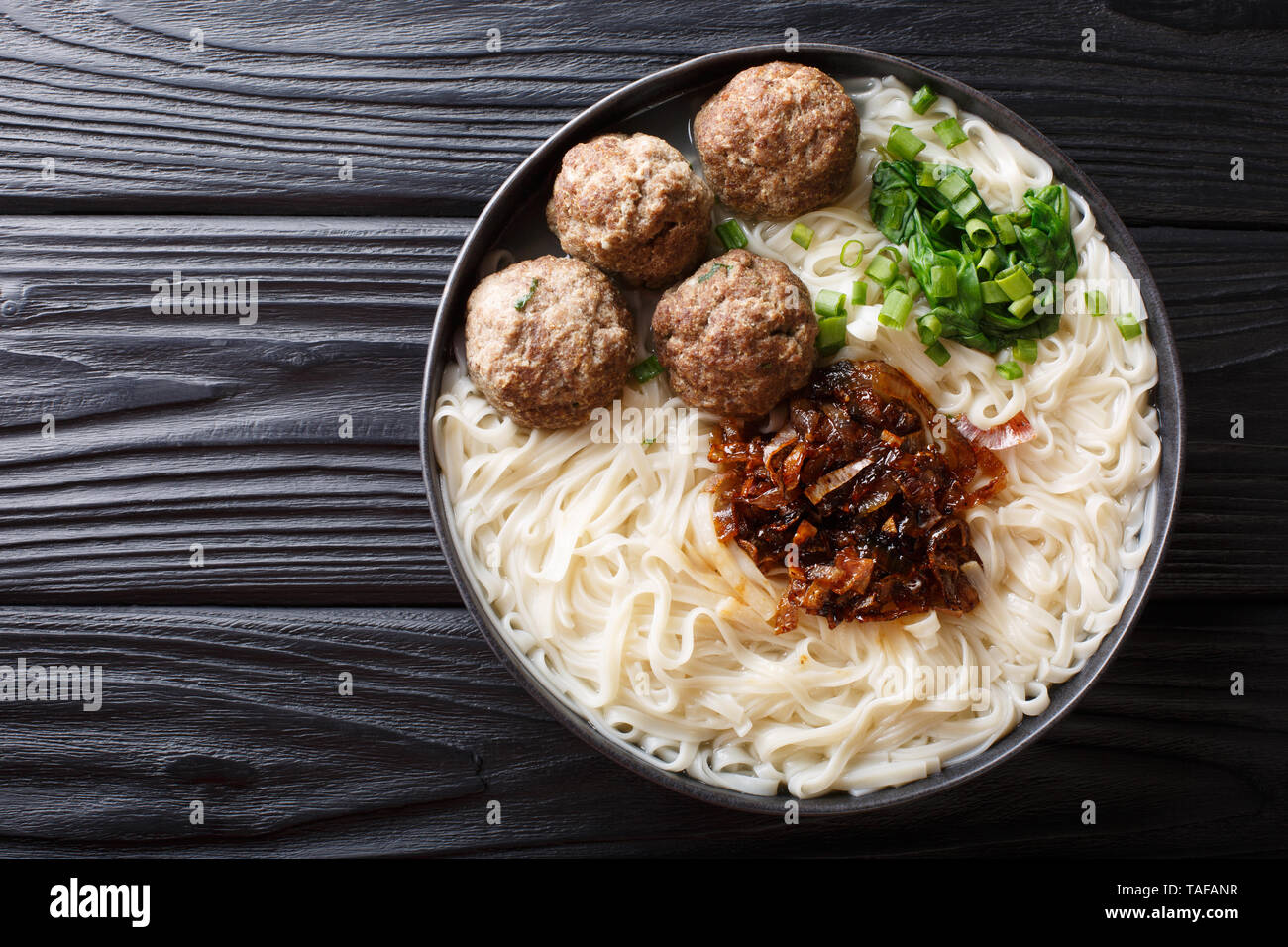 Boulettes de bœuf traditionnel indonésien avec des nouilles, des oignons frits, les verts et le bouillon gros plan sur une assiette sur la table. haut horizontale Vue de dessus Banque D'Images