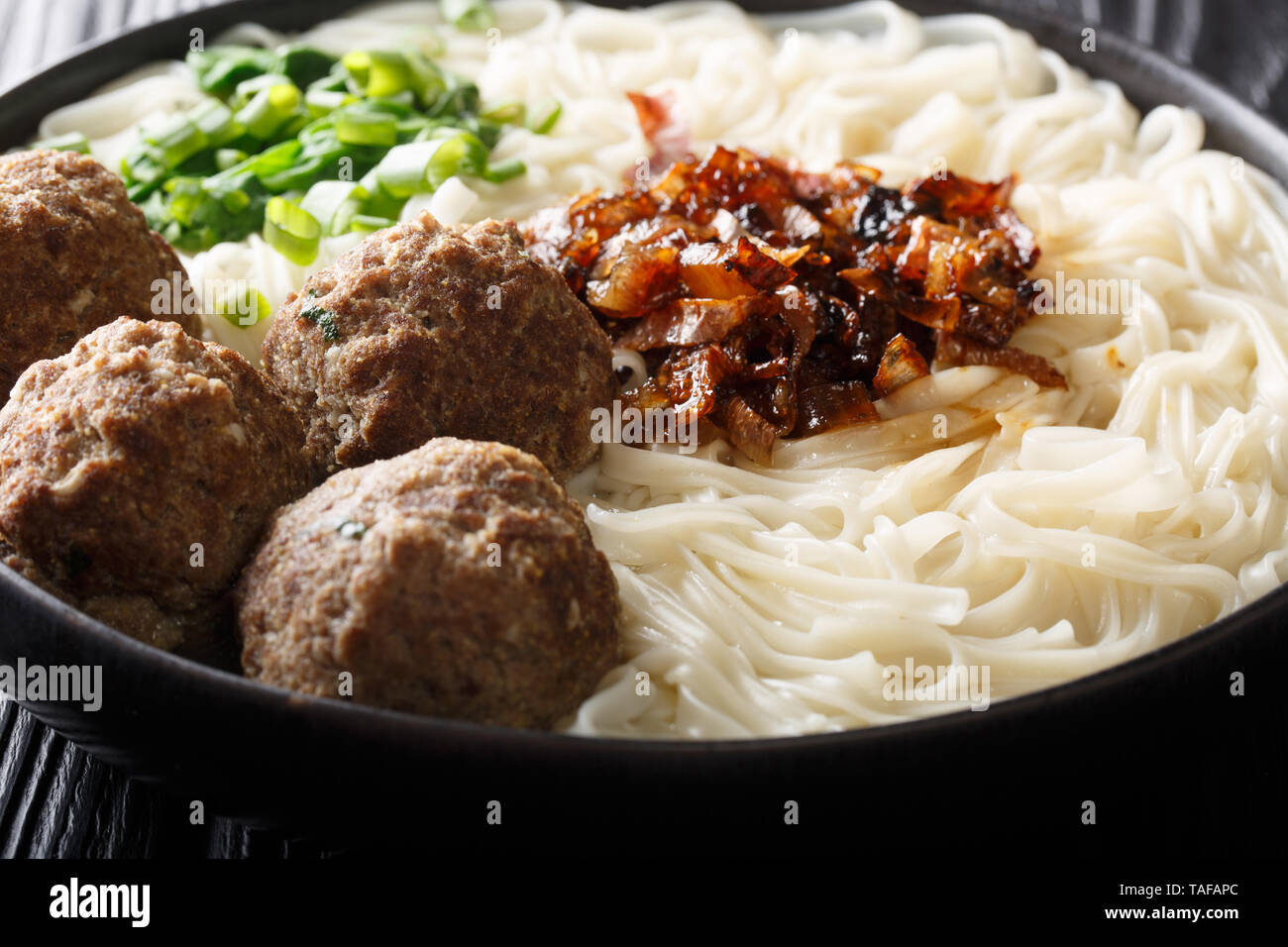 Boulettes de bœuf traditionnel indonésien avec des nouilles, des oignons frits, les verts et le bouillon close-up sur une plaque sur la table horizontale. Banque D'Images