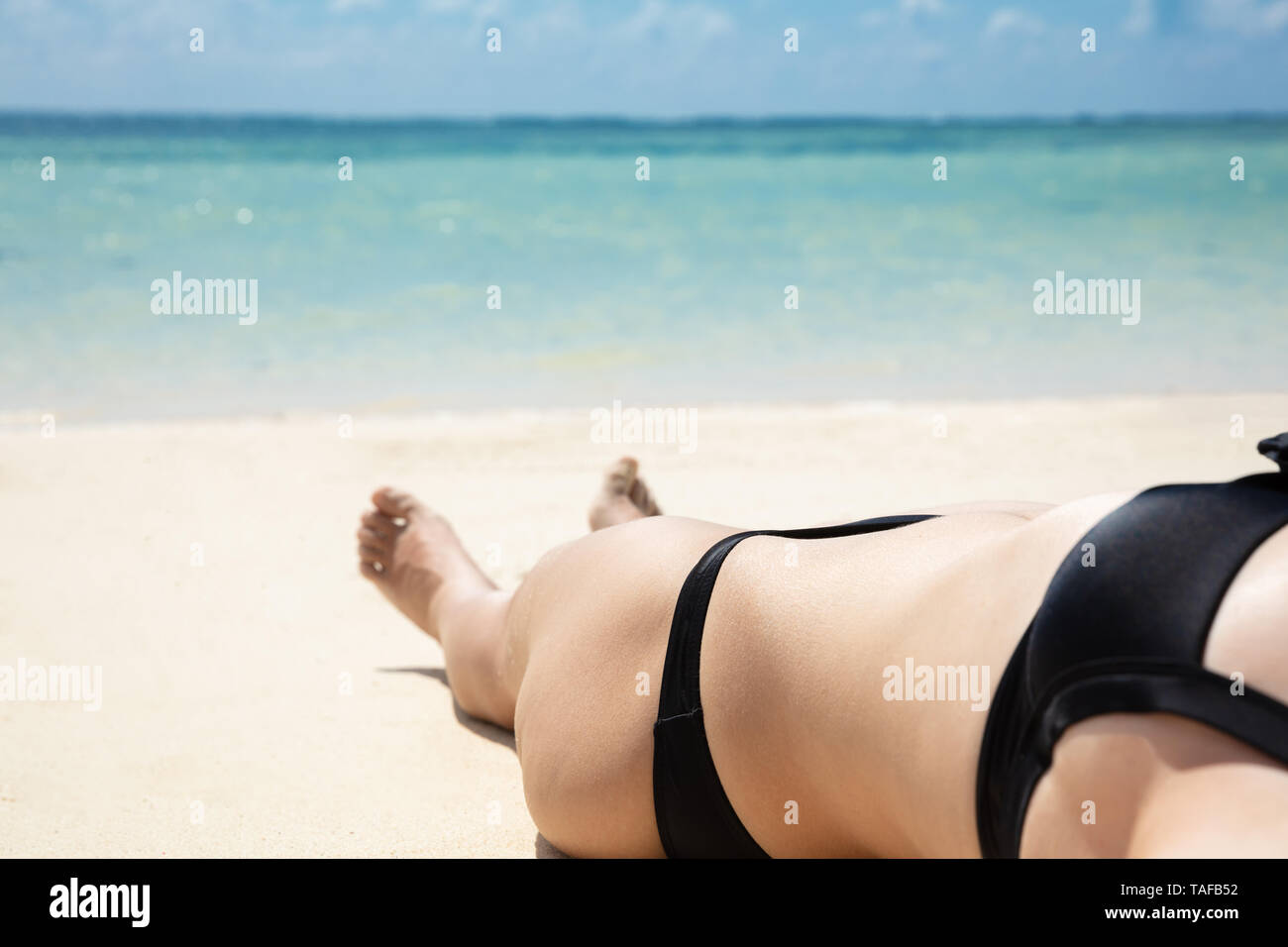 Jeune Femme en bikini noir et lunettes de détente sur une plage de sable près de la mer Banque D'Images