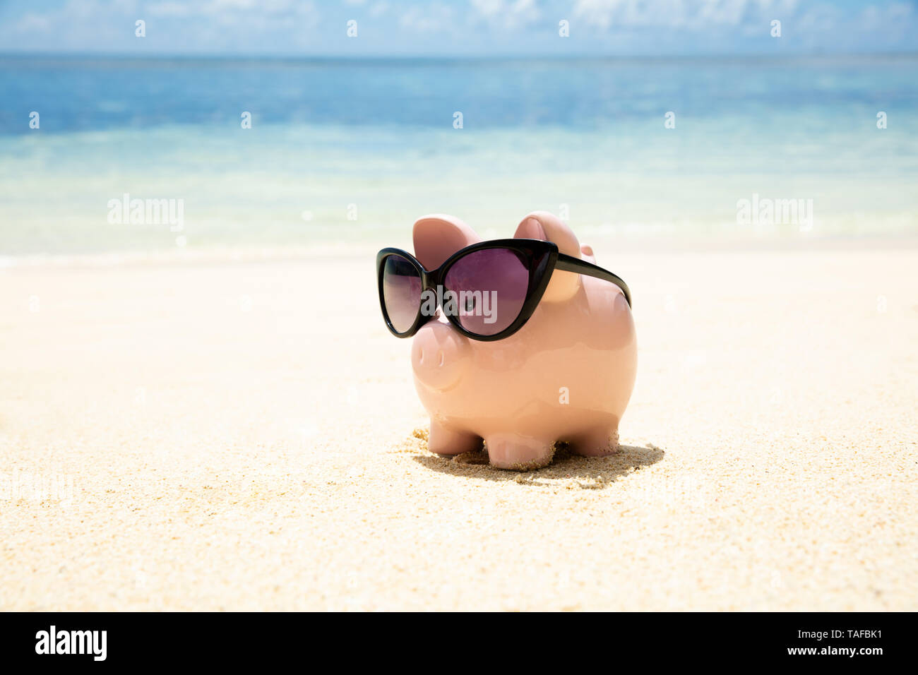 Pink Piggybank portant des lunettes noires sur le sable à la plage Banque D'Images