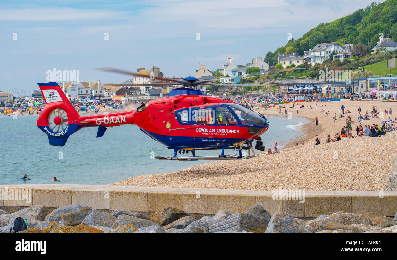 Lyme Regis, dans le Dorset, UK. 25 mai 2019. Devon Air Ambulance hélicoptère atterrit sur la plage bondée à Lyme Regis. L'hélicoptère décolle de la plage bondée avec un patient à bord. Credit : Celia McMahon/Alamy Live News. Banque D'Images