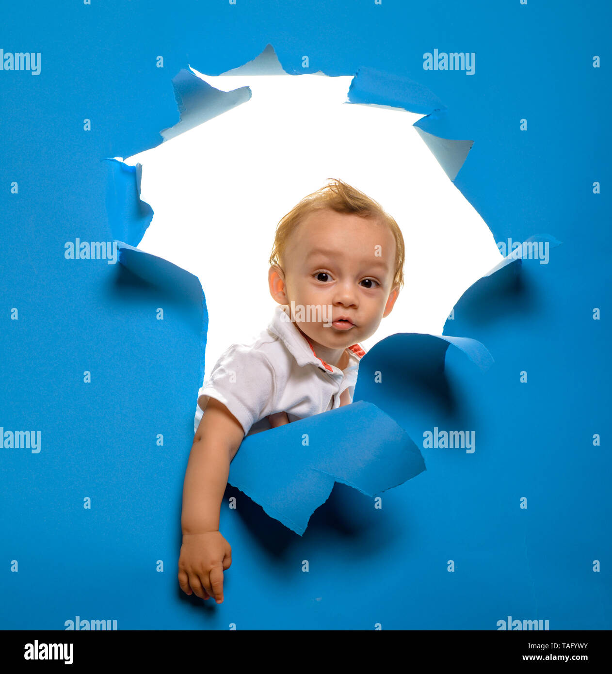 Être curieux. Petit enfant peek par papier déchiré. Petit enfant coupant à travers mur bleu. Garçon enfant curieux regardent par le trou dans le papier. Entrée de sw Banque D'Images