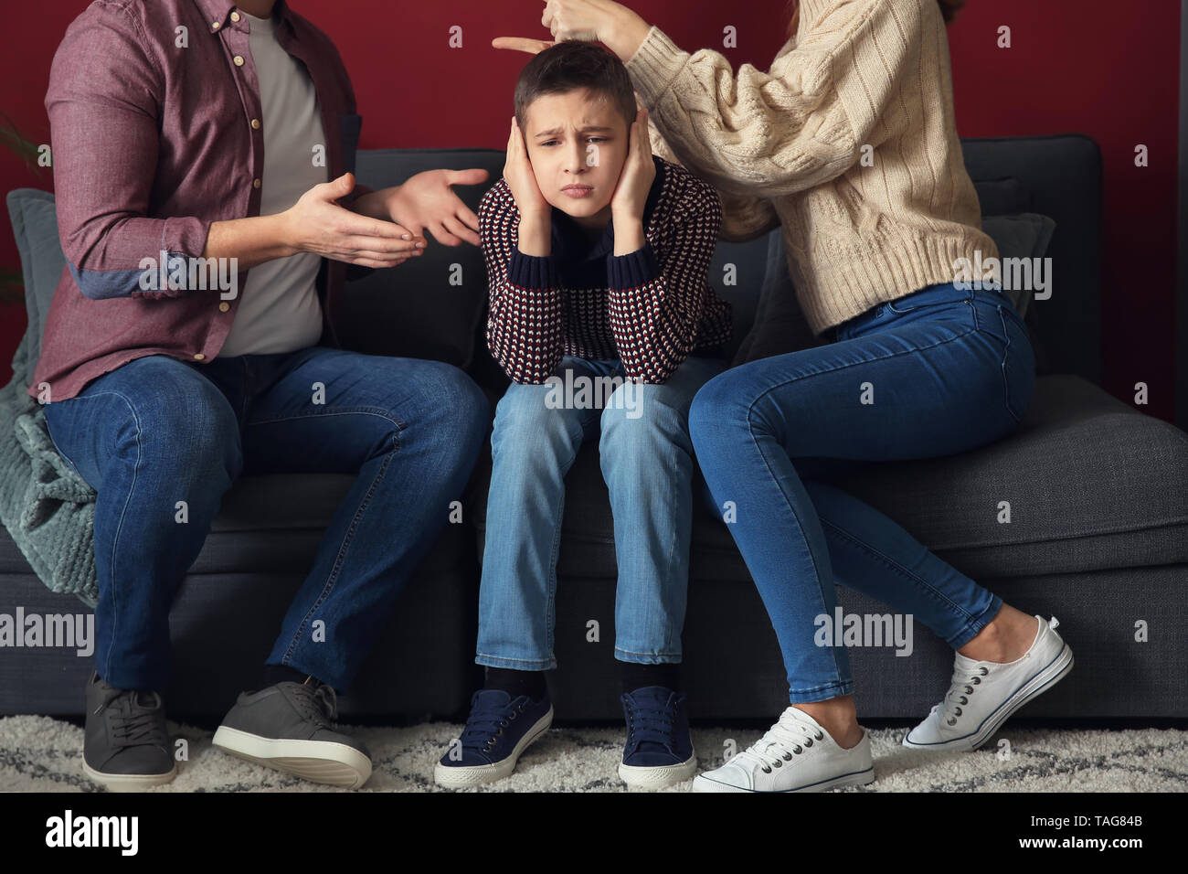 Petit garçon triste couvrant les oreilles pendant que ses parents se disputer à la maison Banque D'Images