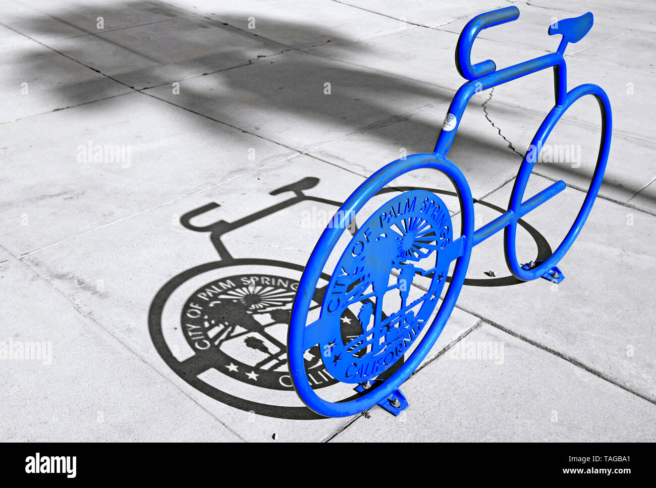 Un stand de vélo bleu avec l'insigne de la ville de Palm Springs Californie et l'ombre d'un palmier sur un trottoir à Palm Springs, Californie, États-Unis. Banque D'Images