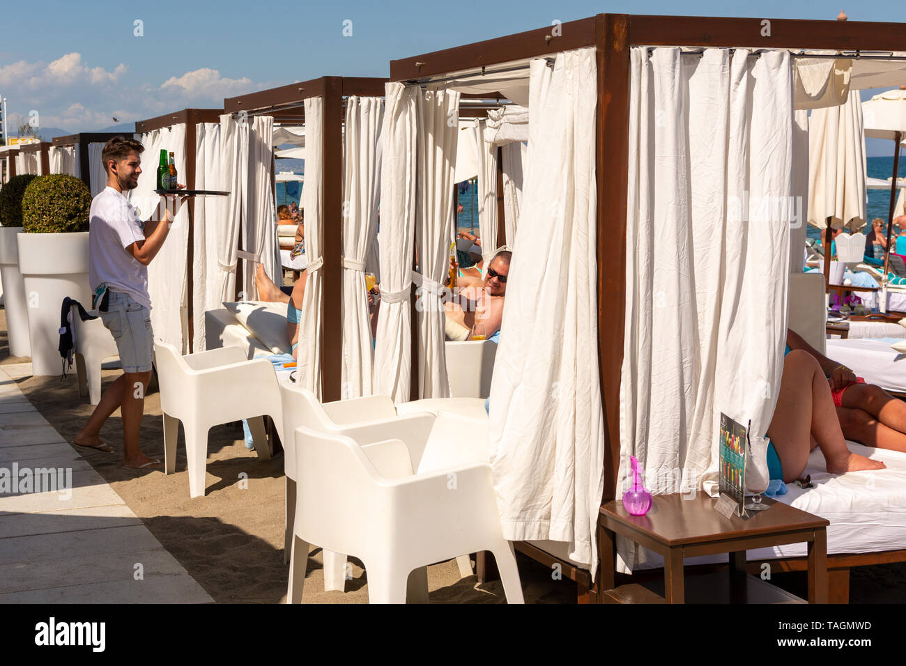 Garçon en blanc au service de clients sur blanc lit haut de gamme-comme des chaises longues sur la plage, Playa Miguel, La Carihuela, Torremolinos, Costa del Sol, Espagne Banque D'Images