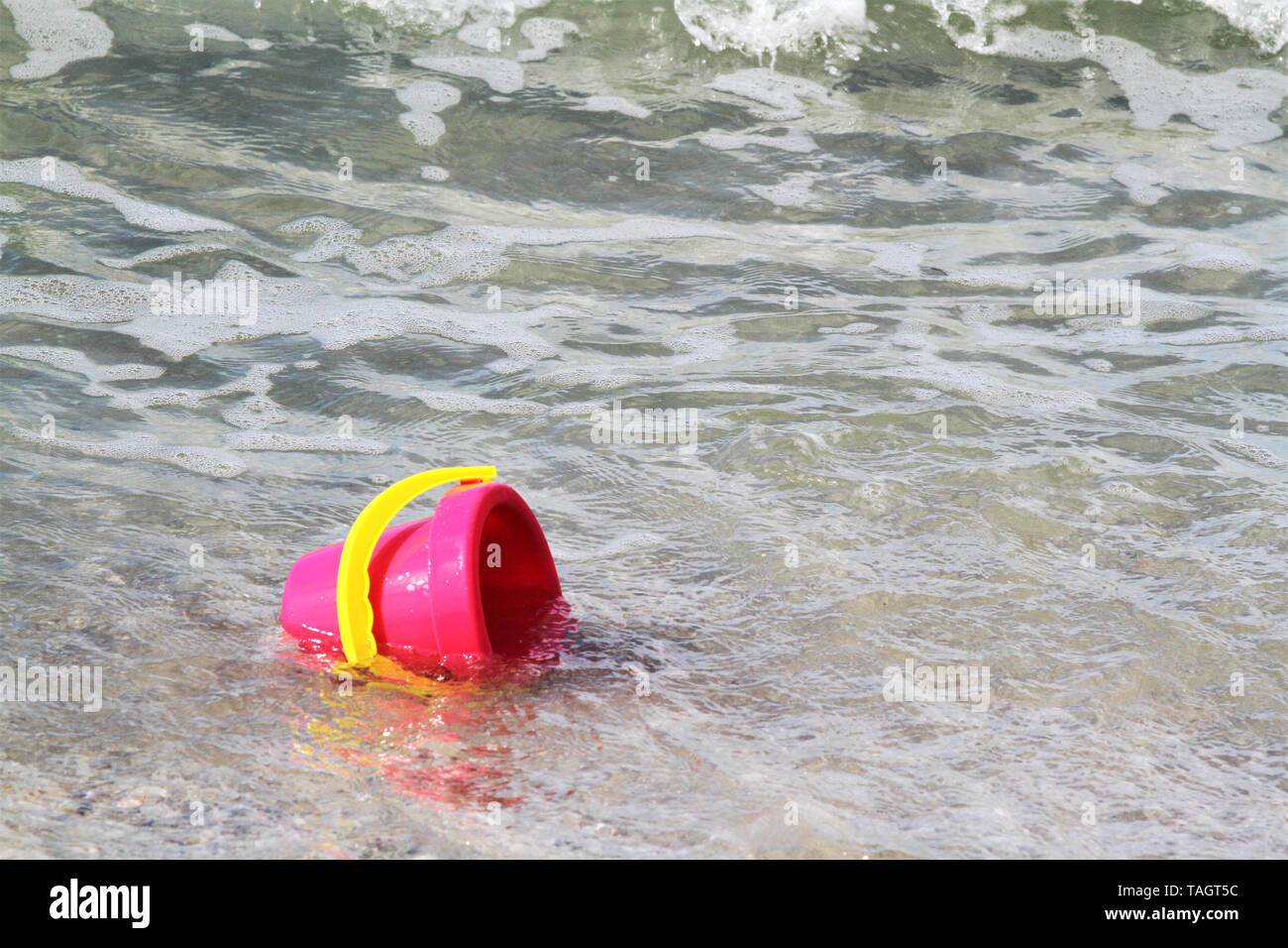 Seau en plastique rose avec poignée jaune sur une plage de sable fin Banque D'Images