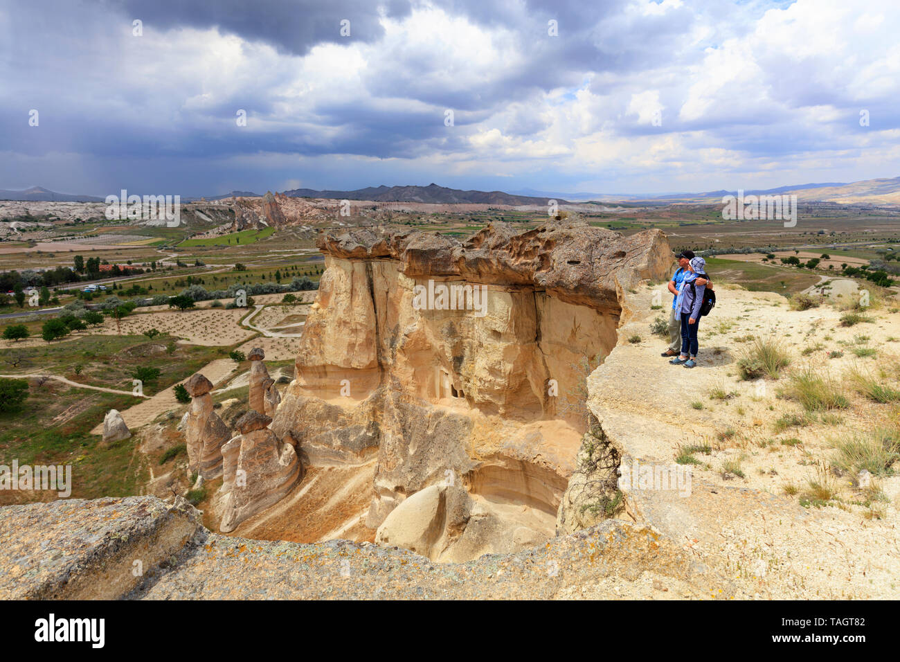 Un jeune couple de touristes avec des sacs sur leur dos se tient sur le bord d'une falaise en Cappadoce et admire l'espace environnant contre le ta Banque D'Images