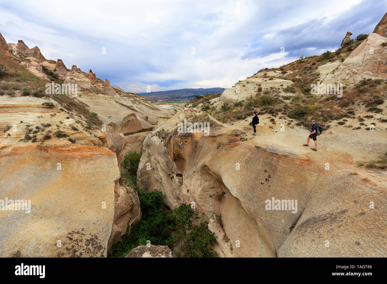 Un jeune couple de touristes inspecte une gorge profonde debout sur le bord d'un canyon en Cappadoce dans le contexte d'un ciel nuageux et la montagne Banque D'Images