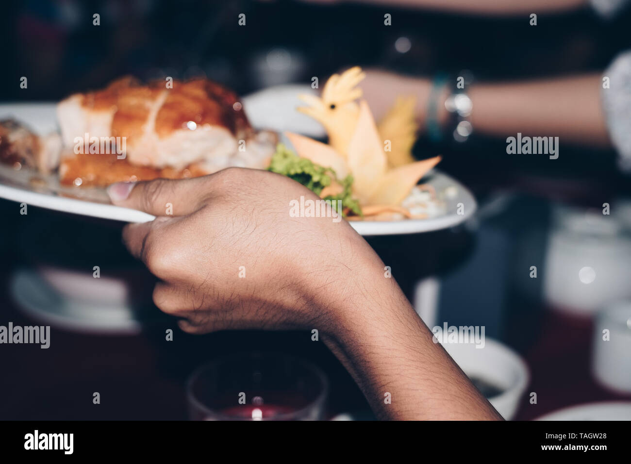Main tenant un plat de poulet d'être passé autour de la table. Focus sélectif. Banque D'Images