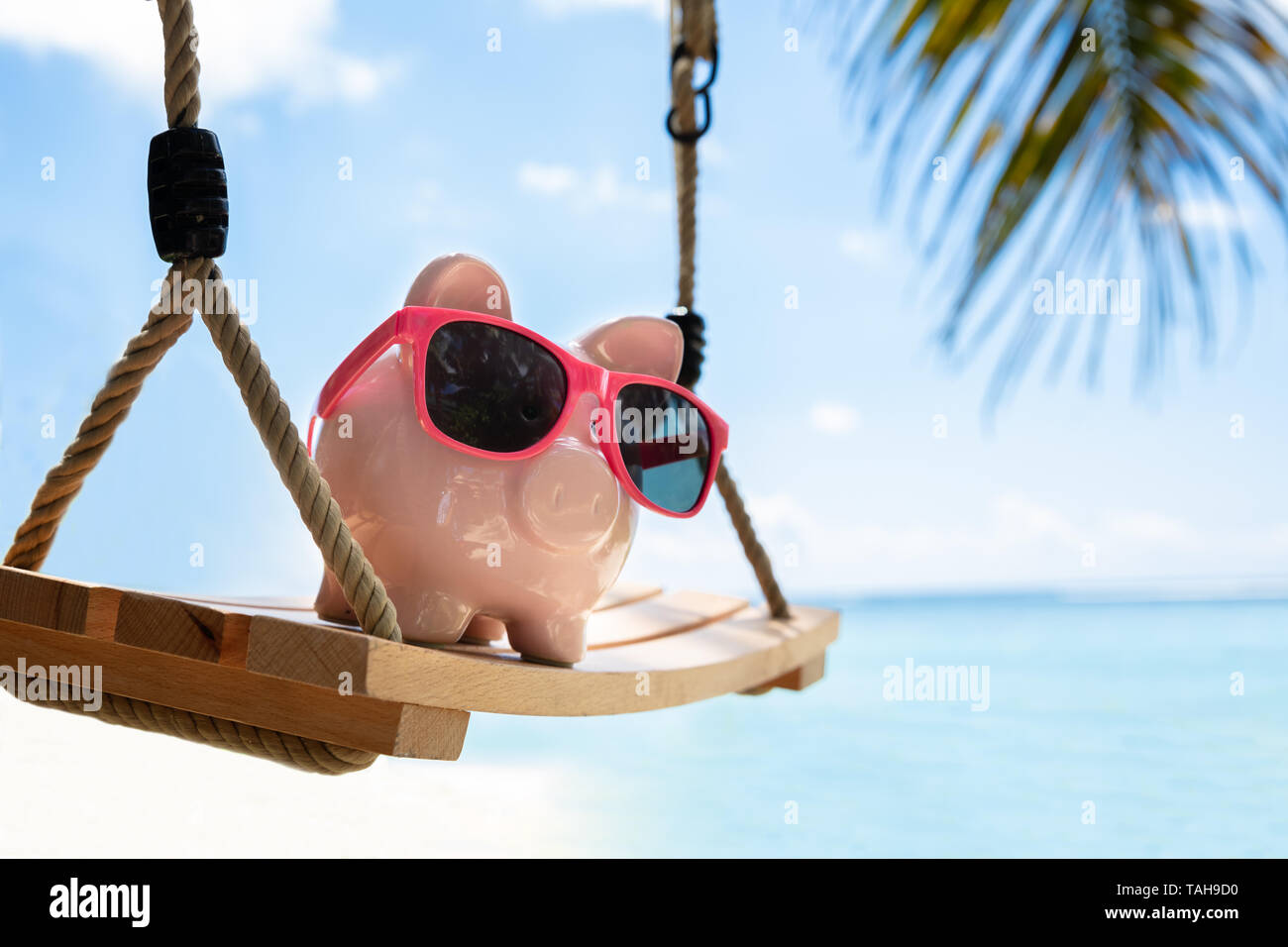 Close-up of Pink Piggybank With Sunglasses sur balançoire en bois At Beach Banque D'Images