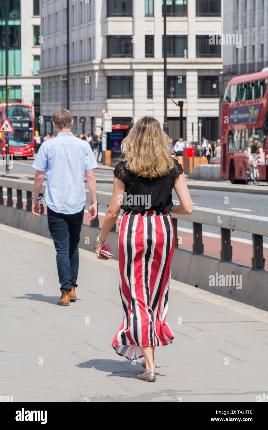 Une femme en rouge et noir dépouillé pantalons de marcher à travers le pont de Londres, London, UK Banque D'Images