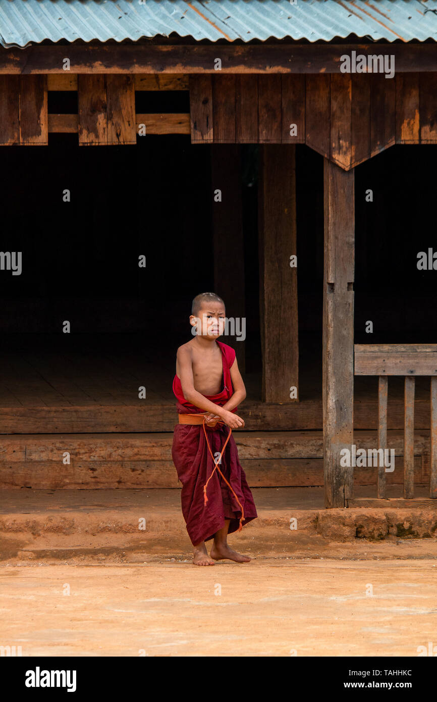 Un jeune garçon rejoint ses robes de moine bouddhiste rouge à côté de son monastère. Banque D'Images