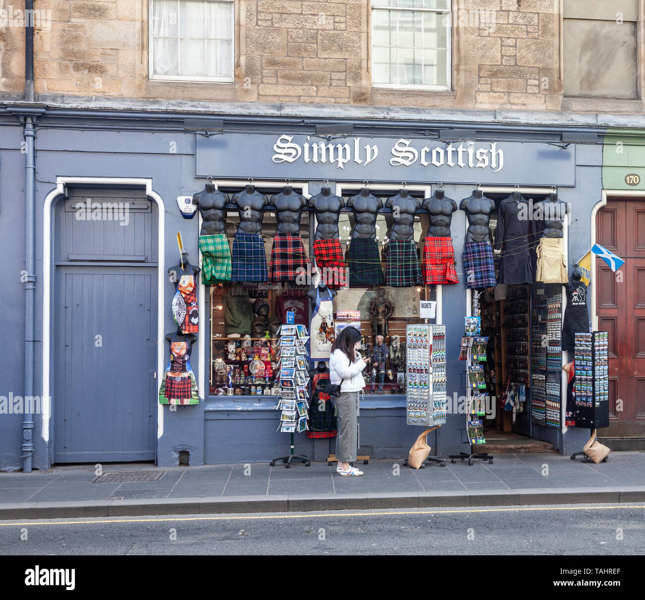 Une jeune femme contrôler son téléphone à l'extérieur tout simplement des Écossais, une boutique vendant des souvenirs, des Écossais dans le Royal Mile / High Street, dans la vieille ville de Edinbu Banque D'Images