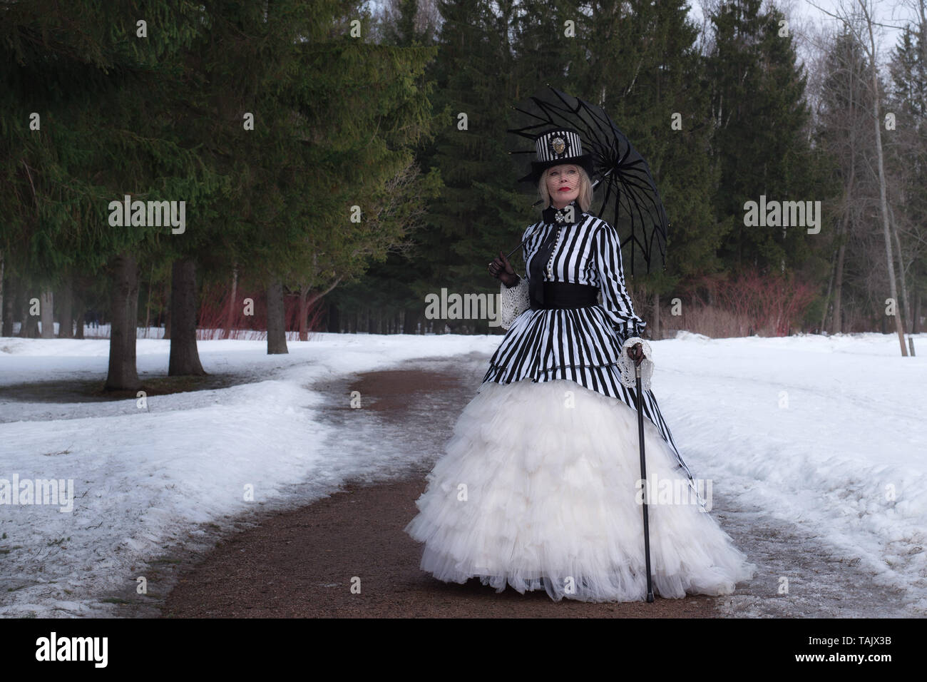 Femme âgée dans une robe gothique dans un chapeau avec un parapluie noir sur la nature en hiver Banque D'Images