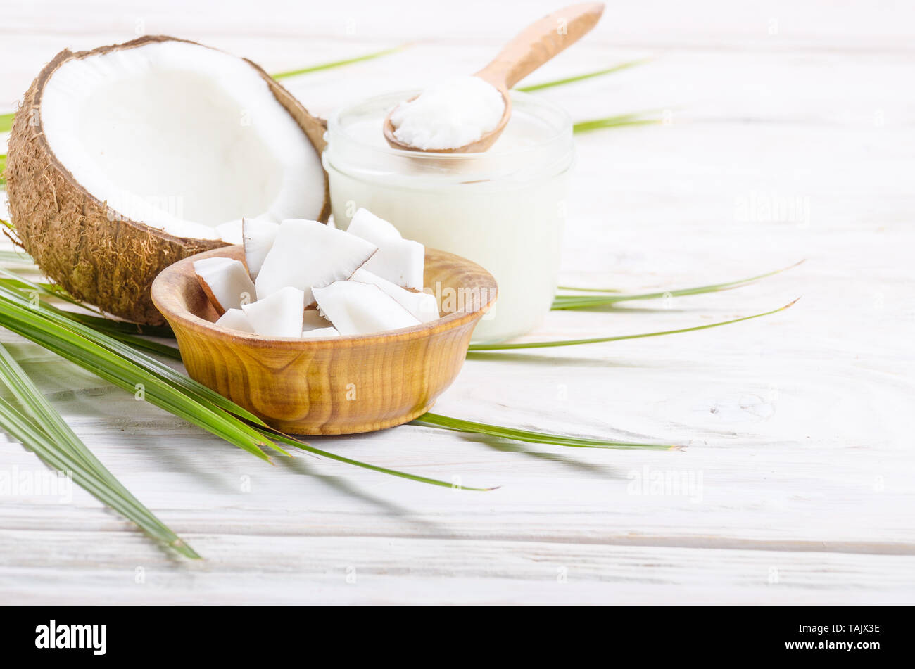 Coque de noix de coco huile dur dans un bocal en verre et de noix de coco en morceaux dans un bol sur la table en bois blanc Banque D'Images