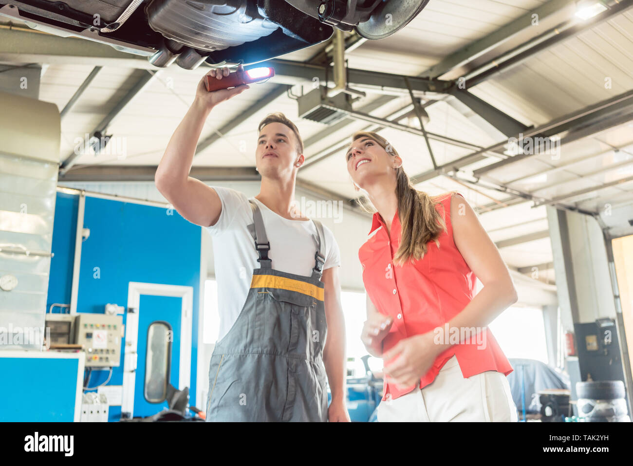Faible angle de vue d'un mécanicien automobile expérimenté, contrôler le disque de disques de frein de la voiture d'un client de sexe féminin dans un atelier de réparation automobile moderne Banque D'Images