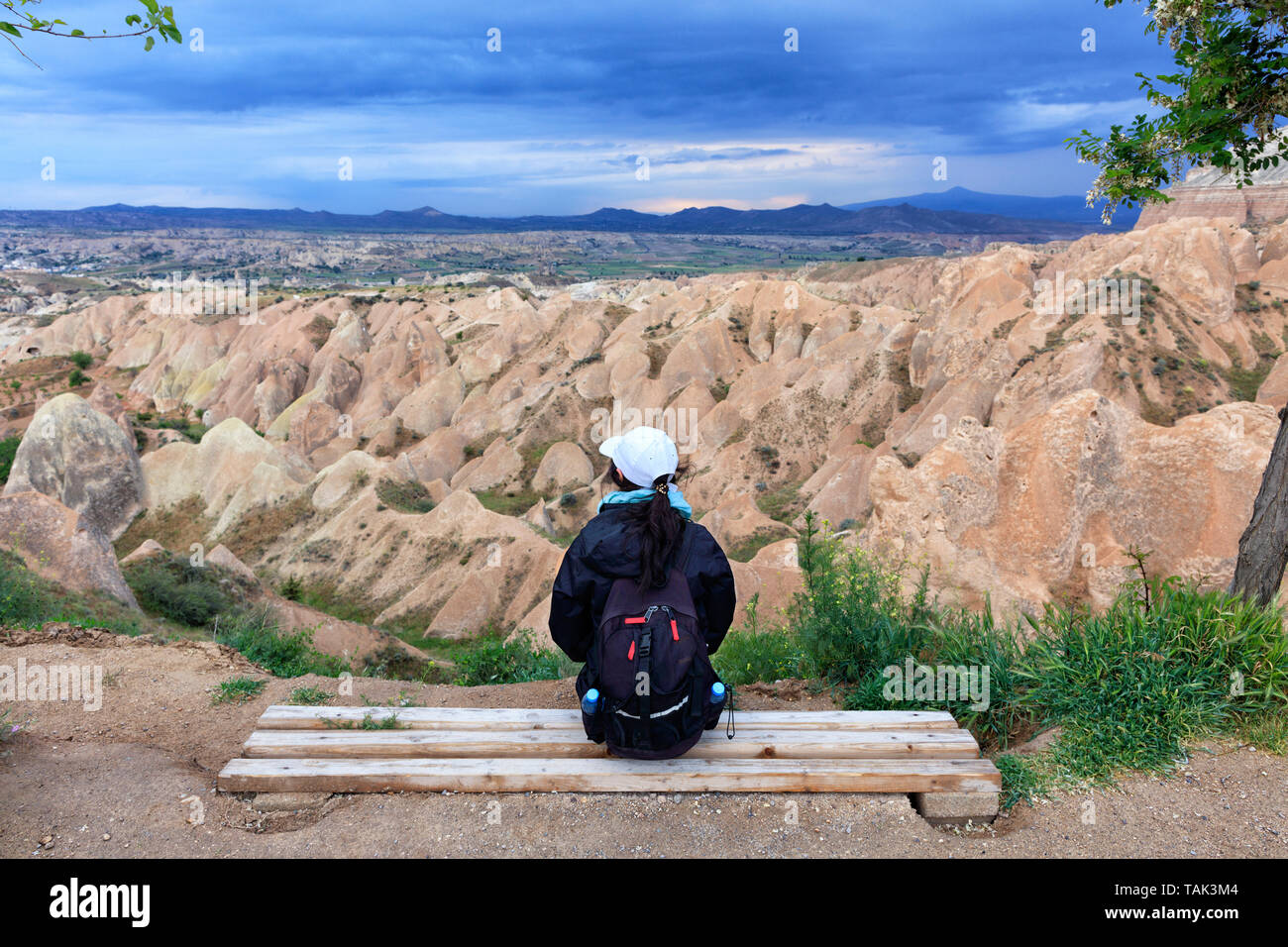 Une jeune fille avec un sac à dos de touriste est assis sur un banc en bois et regarde les montagnes, ravins et un ciel d'orage. Banque D'Images