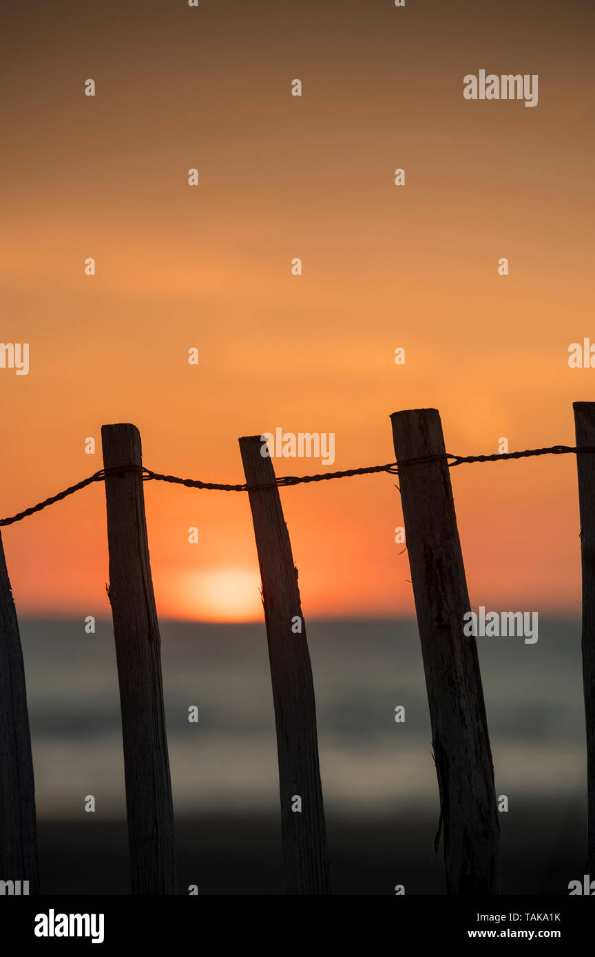 Le coucher de soleil vu à travers une clôture sur une plage de sable Banque D'Images