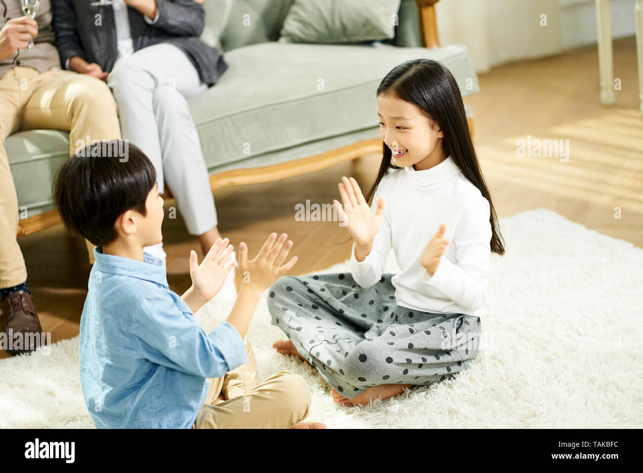 Deux enfants asiatiques mignon petit frère et sœur assis sur un tapis de jeu jouer avec parent assis sur un canapé à l'arrière-plan Banque D'Images