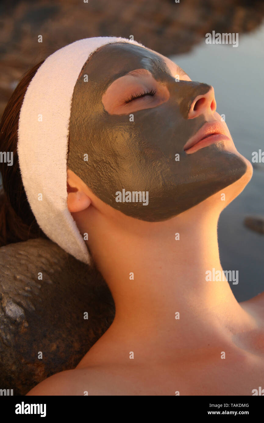Une belle dame avec un masque de boue pour le visage détendu et fixant à la rive de la mer Morte en Jordanie Banque D'Images