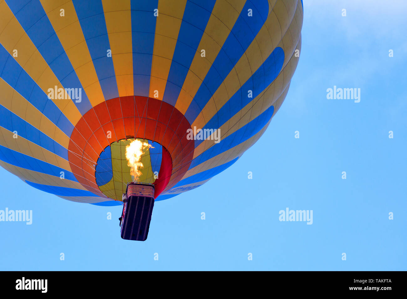 La flamme de feu réchauffe l'air dans un beau motley jaune-bleu ballon et soulève un panier de touristes dans le ciel bleu, vue de dessous. Banque D'Images