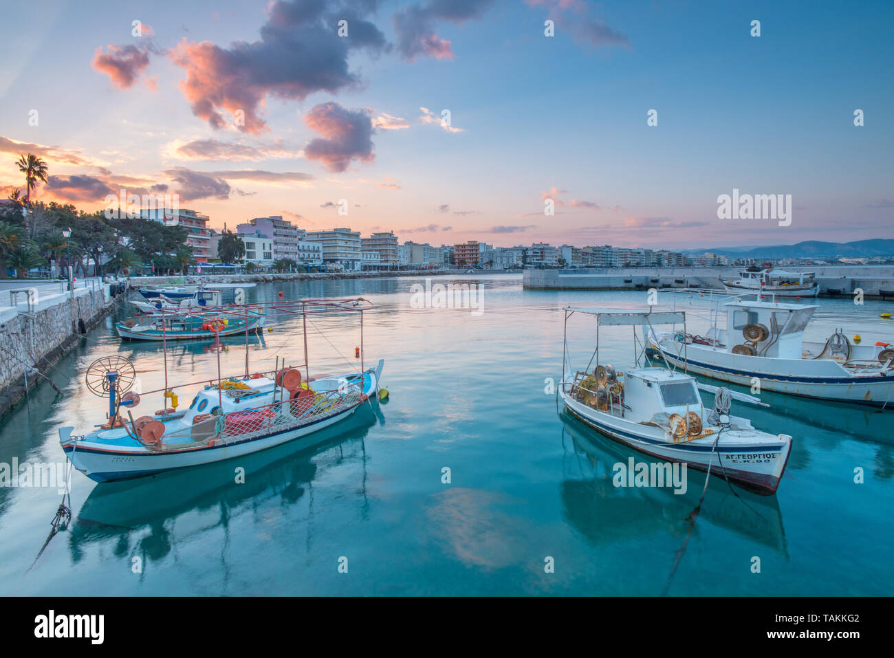 Lever de soleil coloré le long de la promenade et du port à Loutraki, Grèce. Ciel peint sur les bateaux de pêche amarrés au quai dans cette ville touristique. Banque D'Images