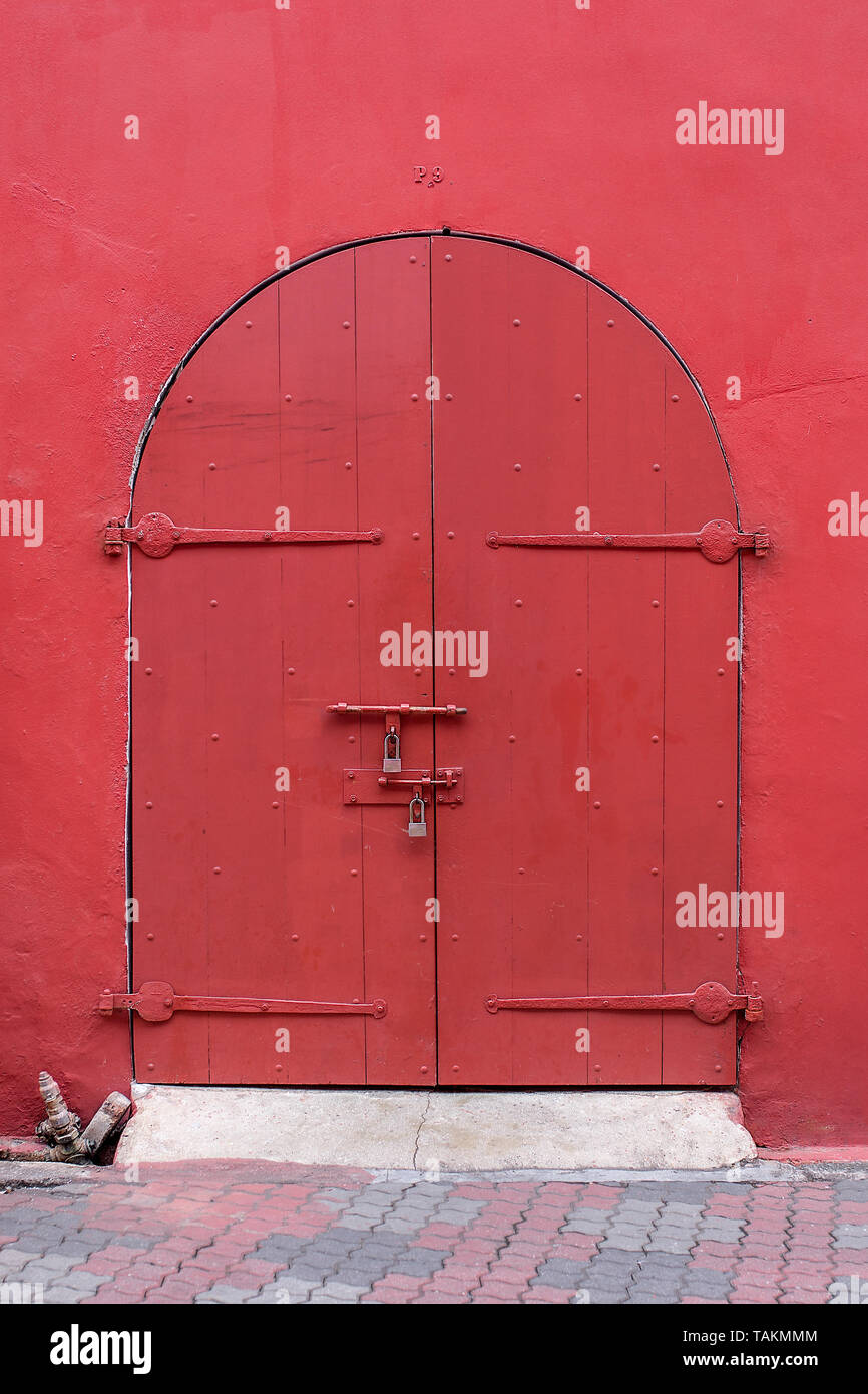 Style ancien porte en bois haut voûté peint en rouge foncé situé dans la paroi rouge. Banque D'Images