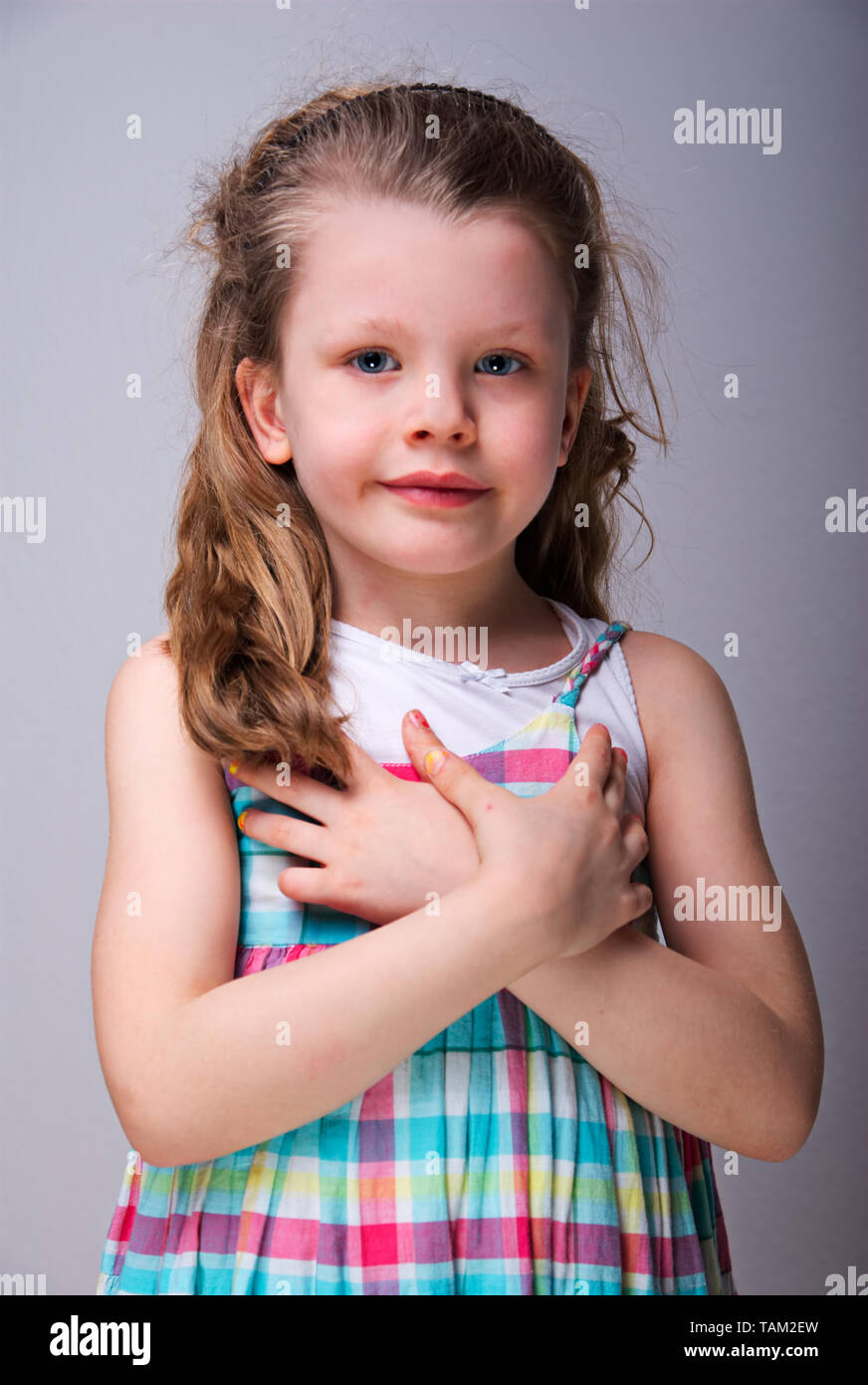 Petite fille blonde aux yeux bleus porte une robe et les croisements de mains sur la poitrine Banque D'Images