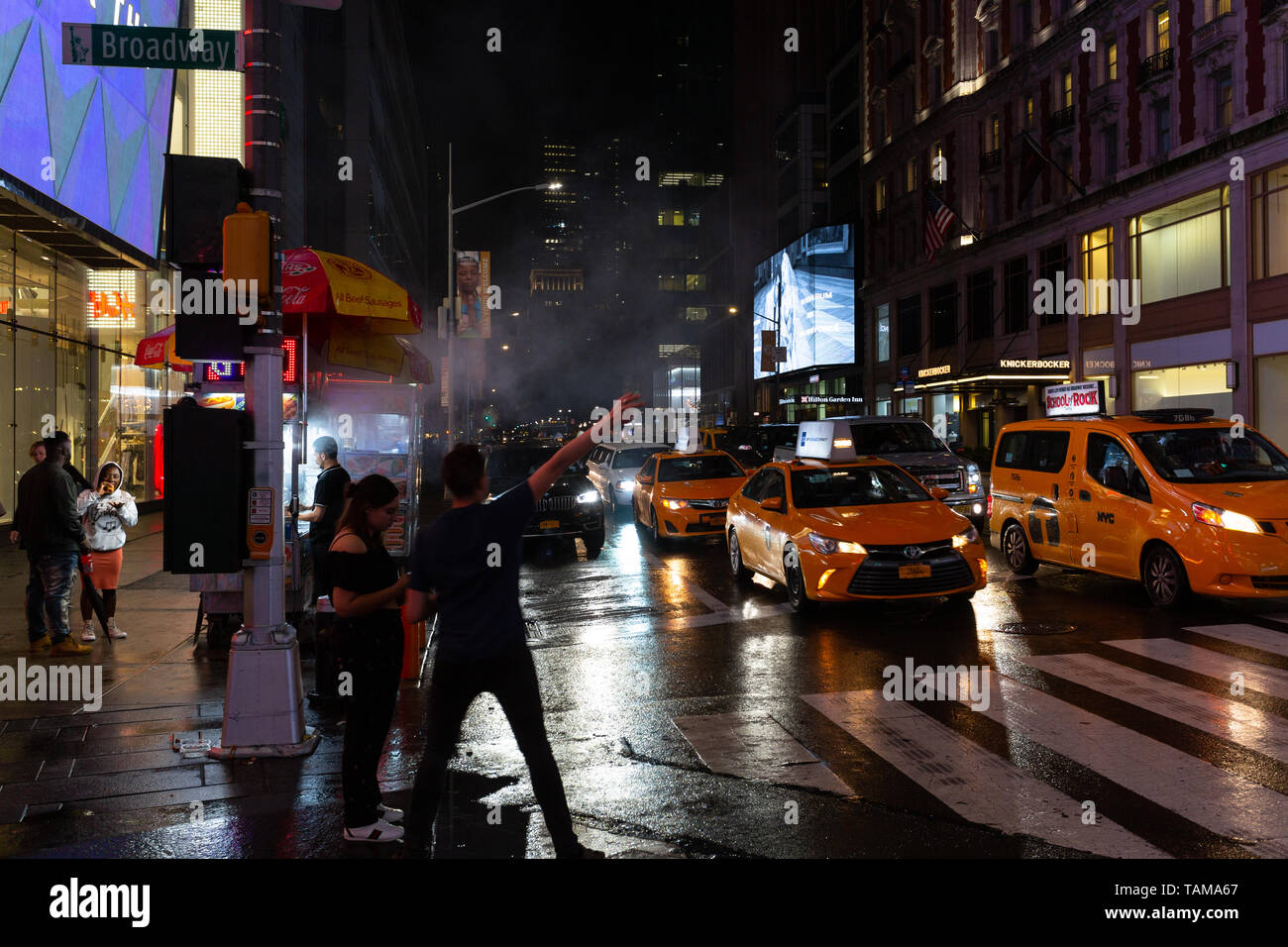 L'homme sur trottoir appelant à l'un des nombreux taxis jaunes à l'extérieur de Times Square - New York City Banque D'Images