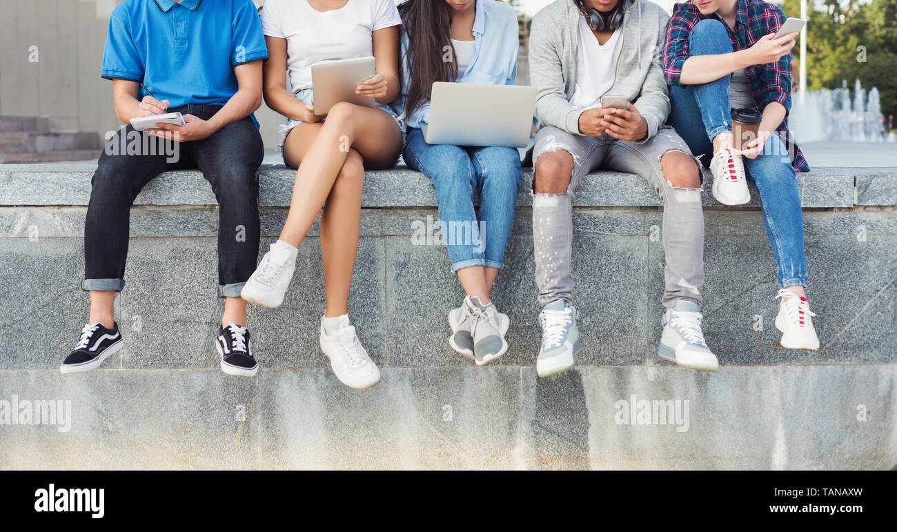 Société d'amis adolescents assis à l'extérieur et à l'aide de gadgets numériques Banque D'Images