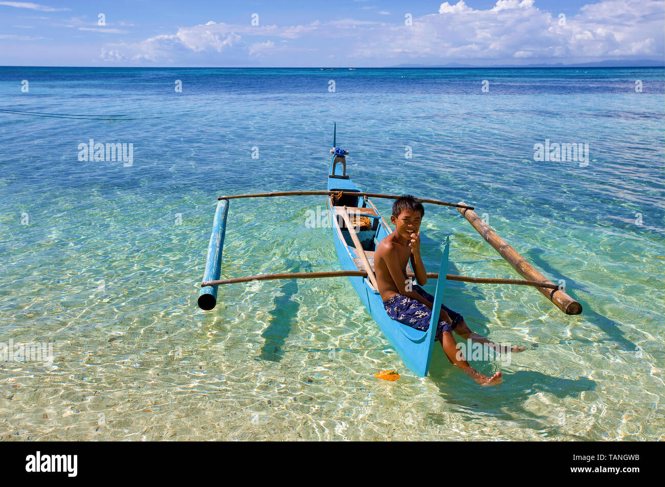 Filipino garçon assis sur un petit bateau outrigger à Bounty beach, Malapascua Island, Cebu, Philippines Banque D'Images